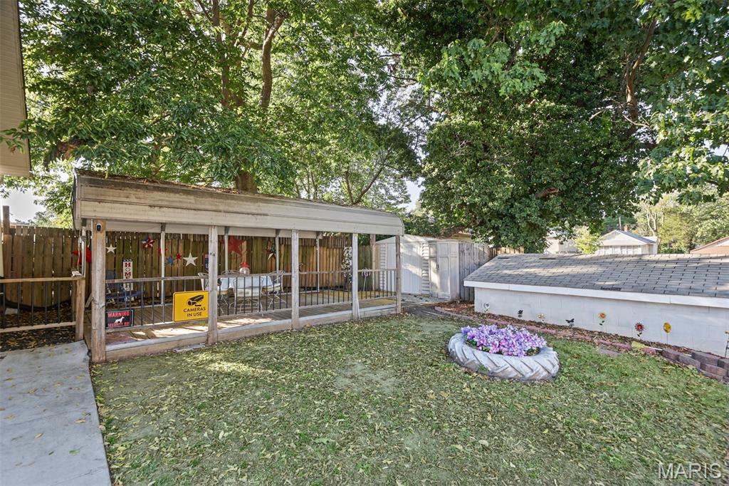 Backyard with a covered patio, fenced lawn, sheds, mature trees, and a circular flower bed.