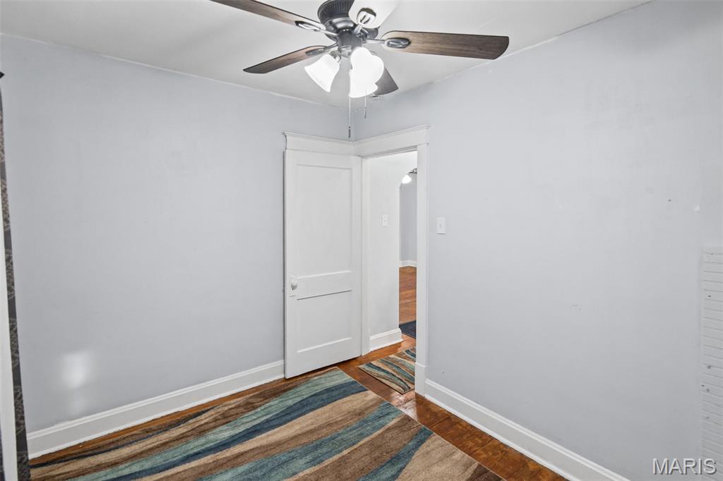 Empty room with ceiling fan, hardwood flooring, striped rug, and open doorway.