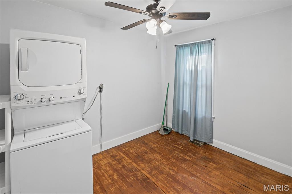 Laundry room with stacked washer and dryer, wood flooring, and a curtained window.