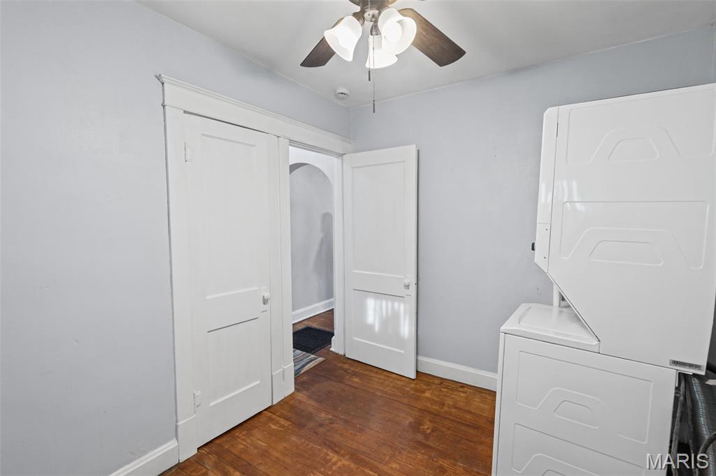 Laundry room with stacked white washer and dryer and hardwood flooring.