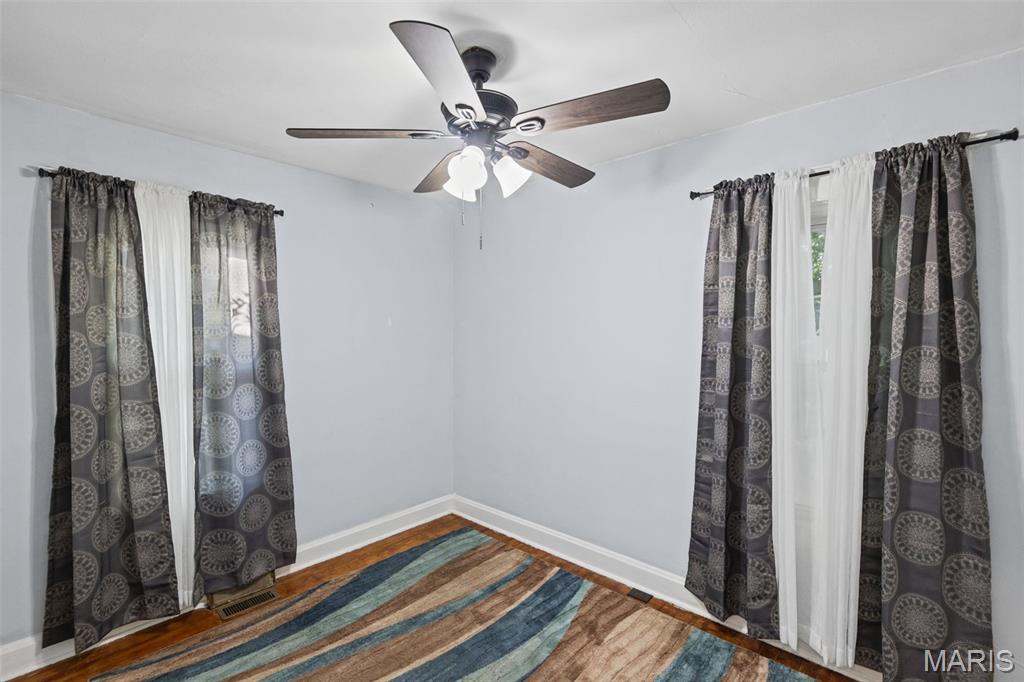 Empty room with patterned curtains, a striped rug, hardwood floors, and a ceiling fan.