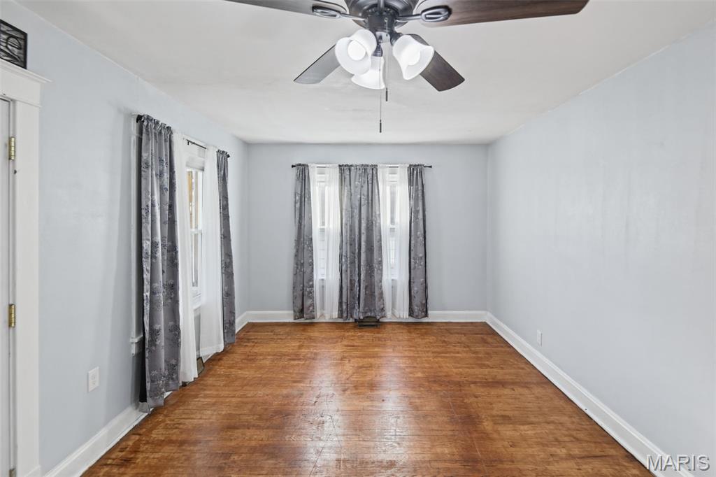 Empty room with hardwood floors, a ceiling fan, and curtained windows.