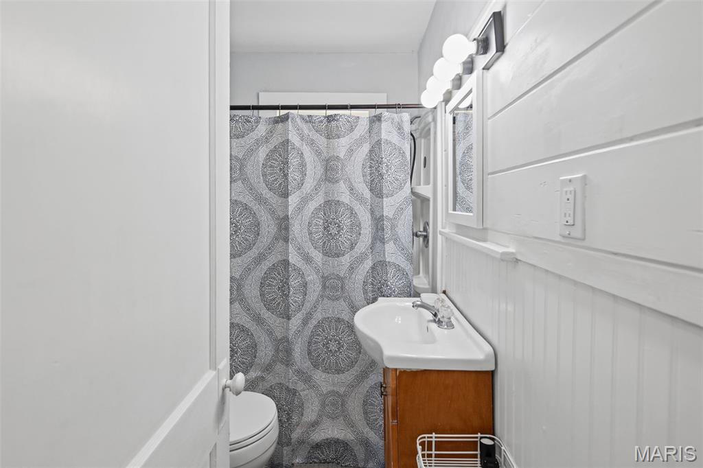 Bathroom with a wood vanity, white sink, and patterned shower curtain.
