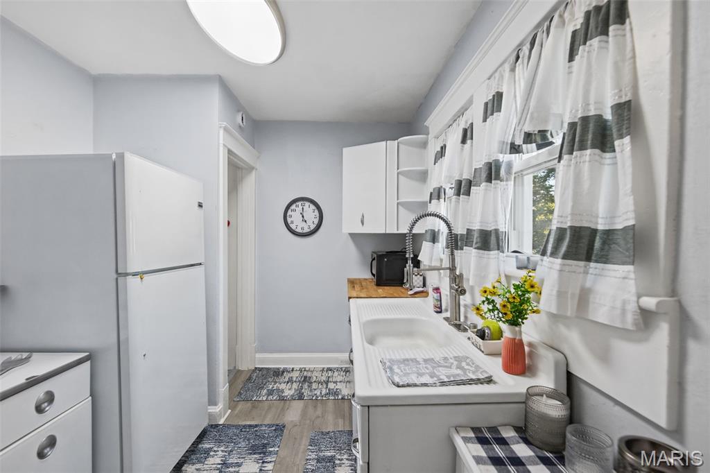 Kitchen with a long white sink beneath striped curtains and a refrigerator opposite.