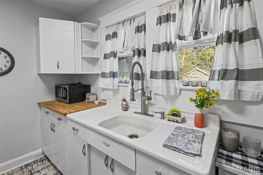 Kitchen with a large white sink, butcher-block counter, and striped curtains.