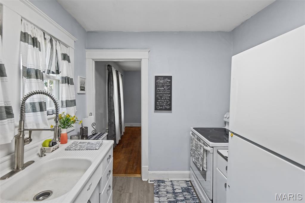 Kitchen with a white sink beneath a curtained window and a white refrigerator and electric range.