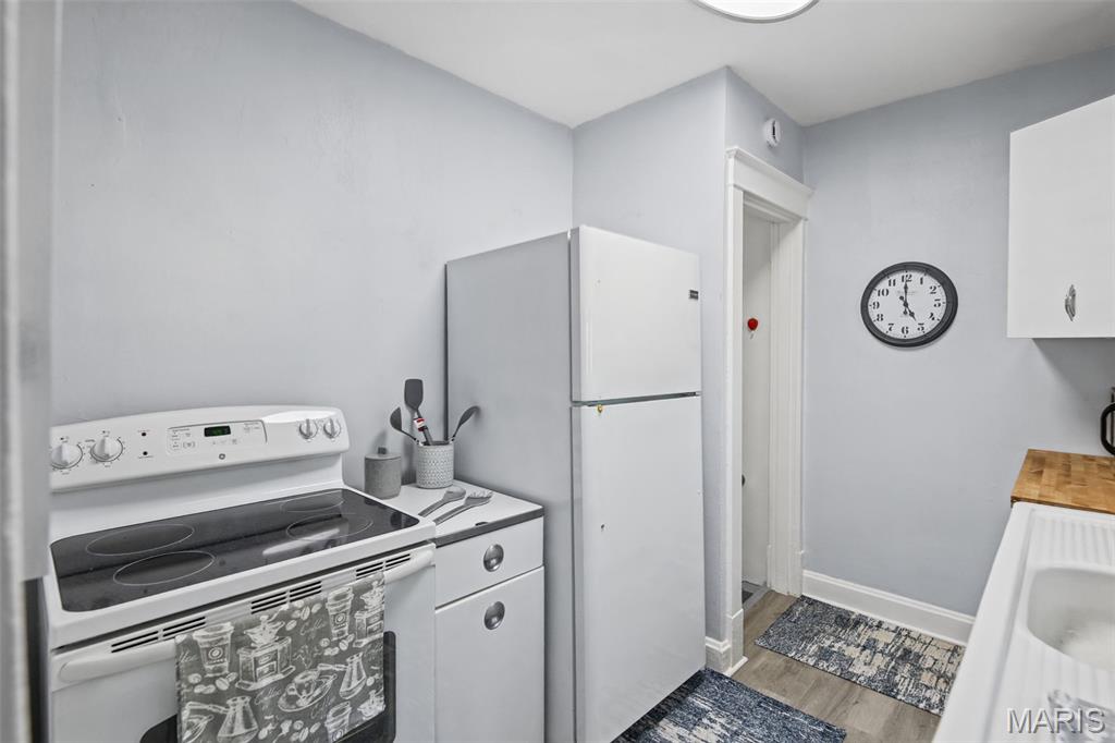 Kitchen with a white electric range and refrigerator beside a doorway and wall clock.