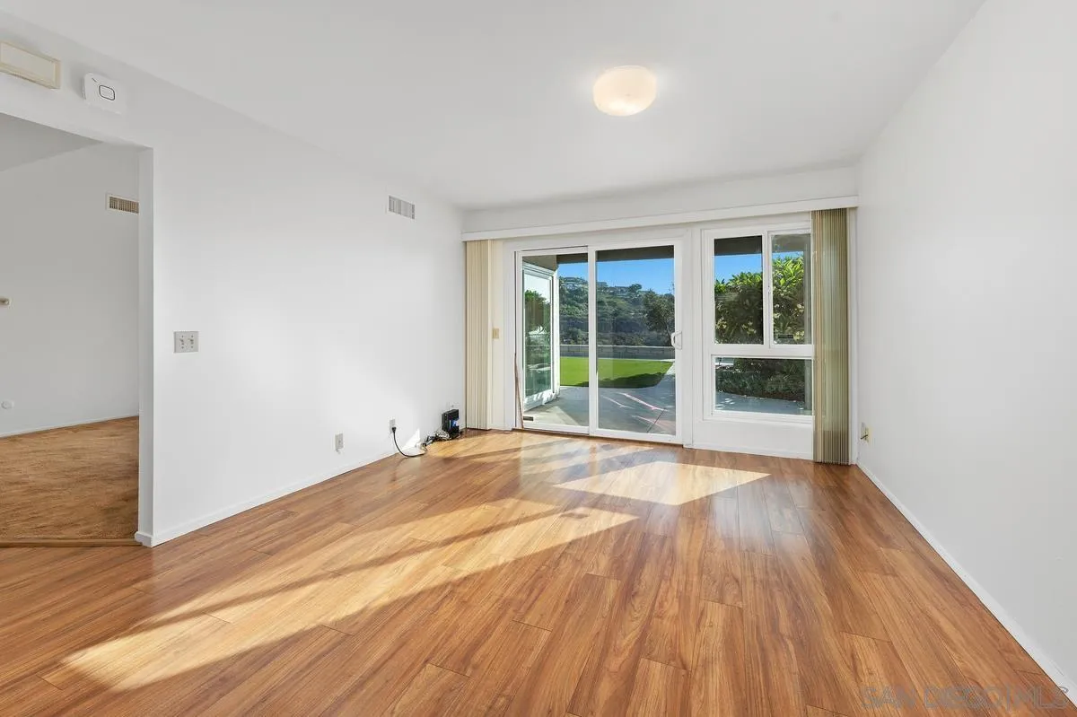 Vacant living room with wood-look floors and sliding glass doors opening to a patio and lawn.