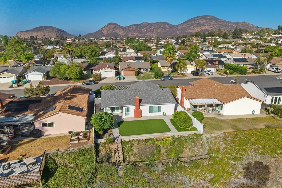 Aerial view of a single-story home with a green lawn, neighborhood rooftops, and mountains beyond.