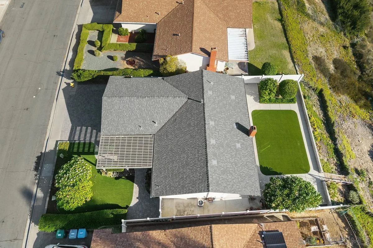 Aerial view of a home with a gray roof, pergola, landscaped lawn, and enclosed artificial turf yard.