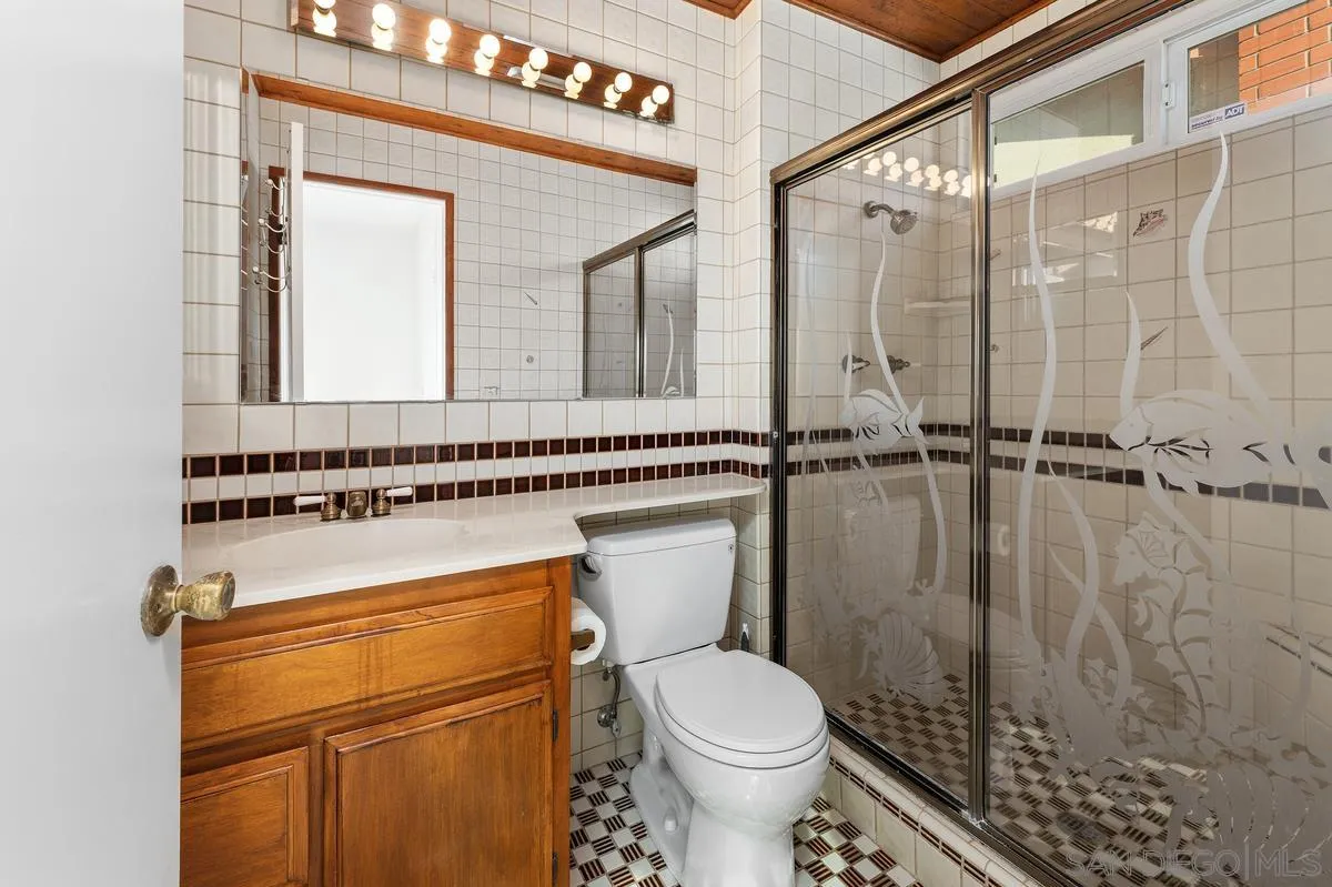 Bathroom with wood vanity and floral-patterned glass shower enclosure.