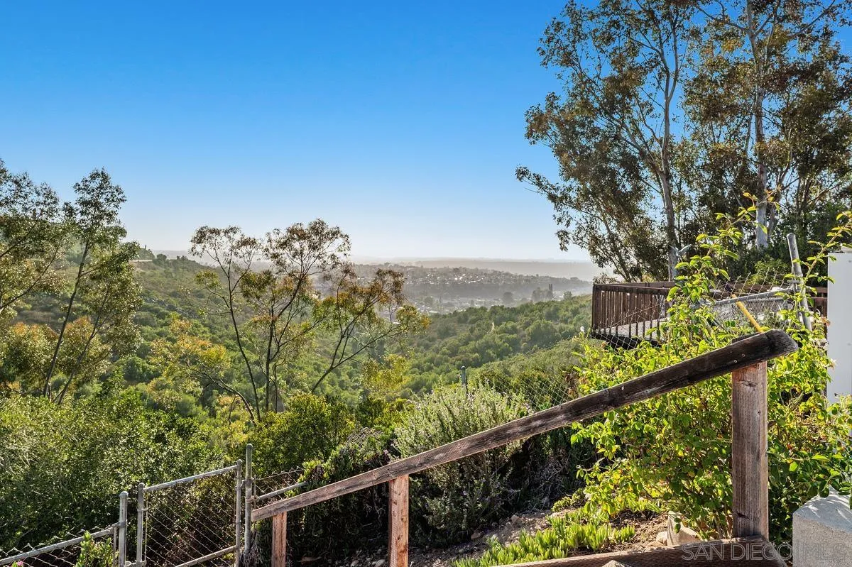 Hillside property view across a green, wooded valley, framed by trees and a wooden fence.