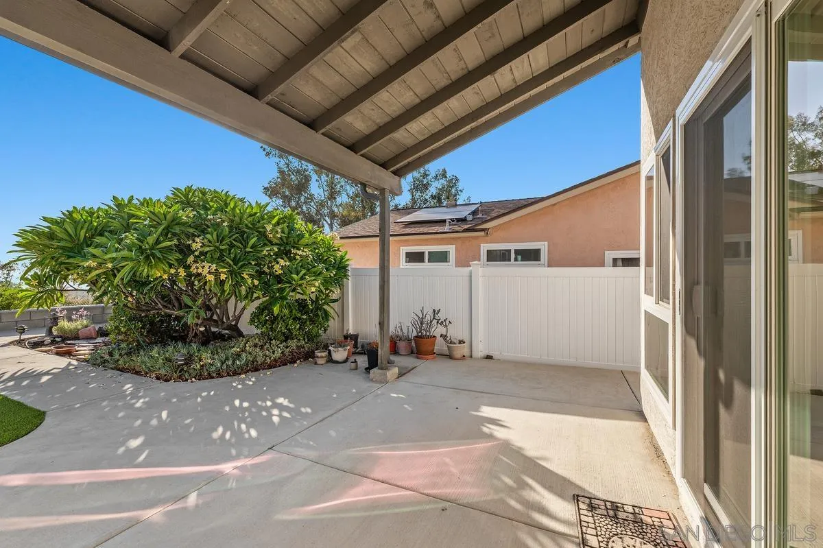 Covered concrete patio with sliding glass doors, a white privacy fence, and a leafy garden bed.
