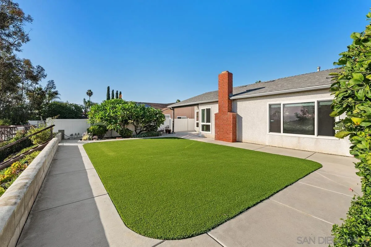 Backyard with a broad artificial-turf lawn, concrete patio, and red-brick chimney.