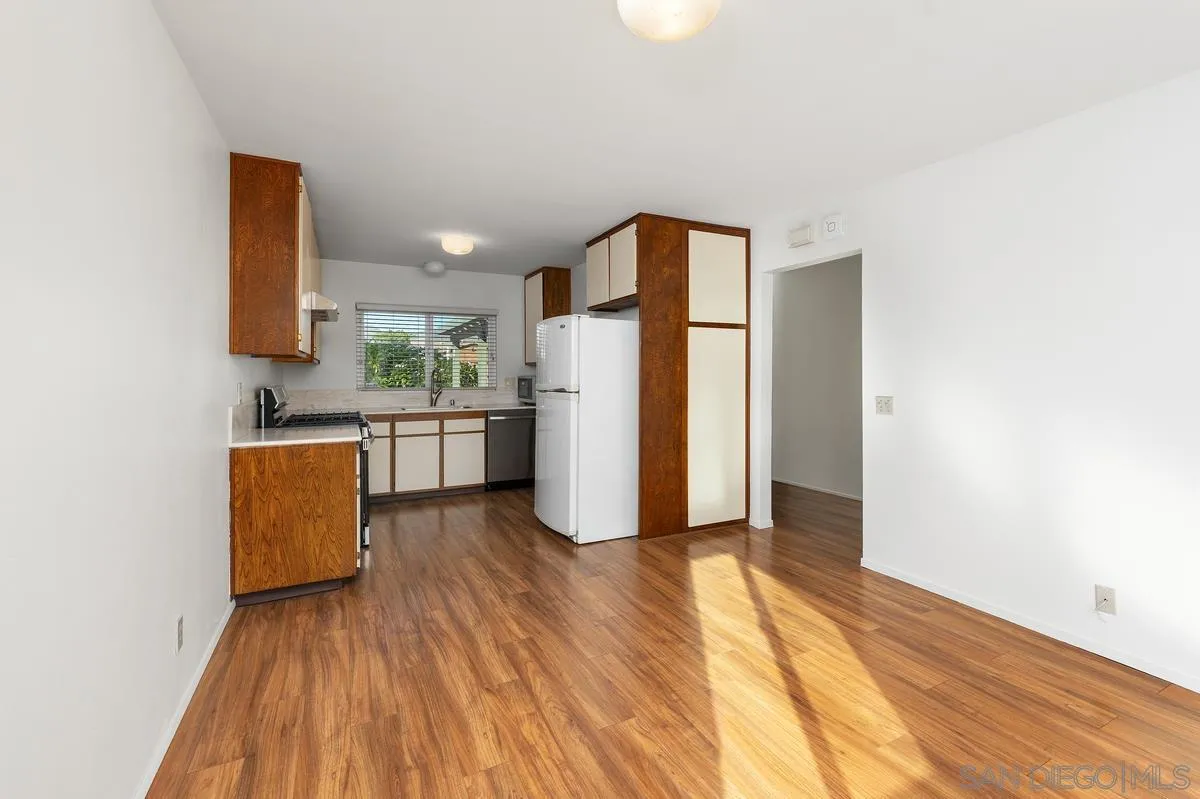 Unfurnished kitchen with wood-tone cabinets, white appliances, and sunlight across the wood-look floor.