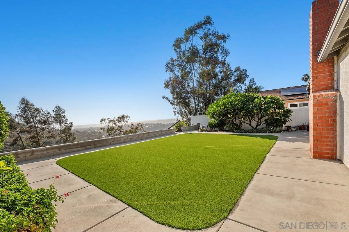 Landscaped yard with a broad green lawn, concrete patio, and hillside views.