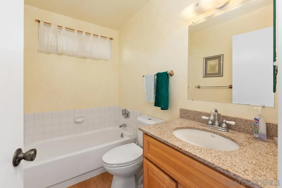 Bathroom with a white bathtub, tiled surround, and wood vanity with a speckled stone countertop.