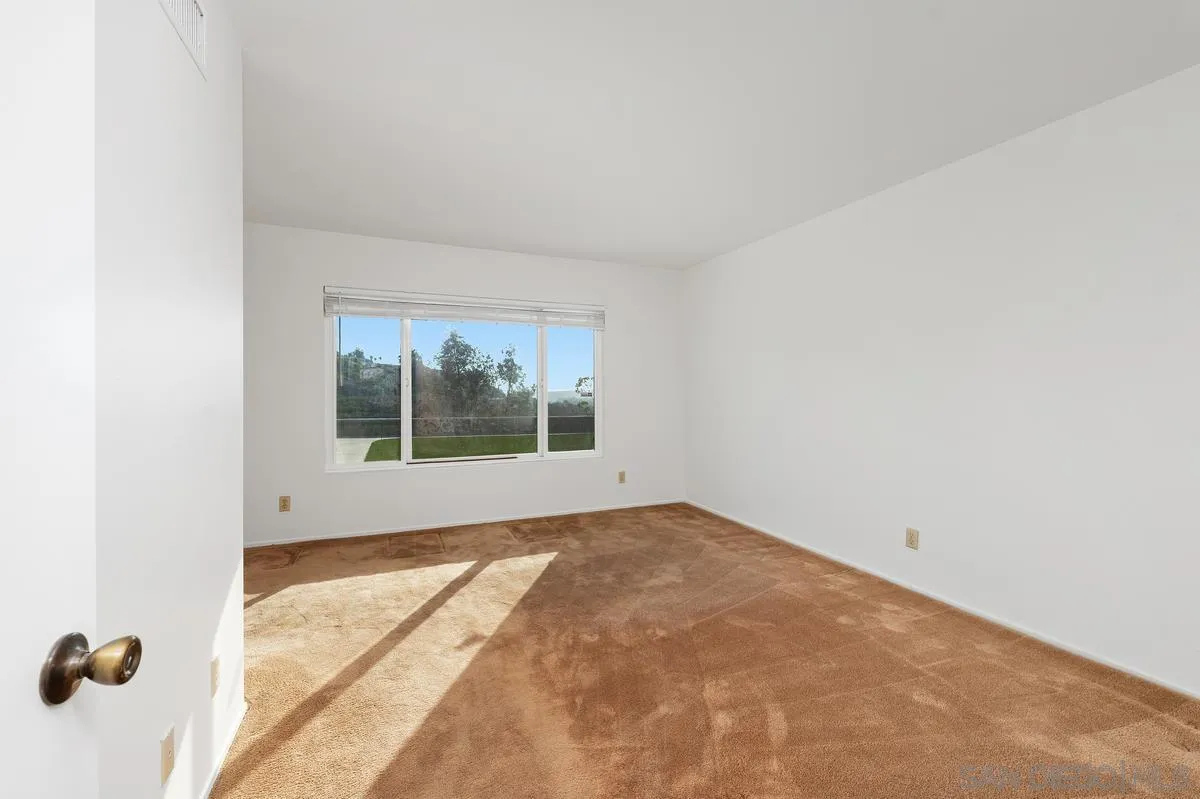 Empty carpeted room with a wide window and sunlight casting long shadows across the floor.