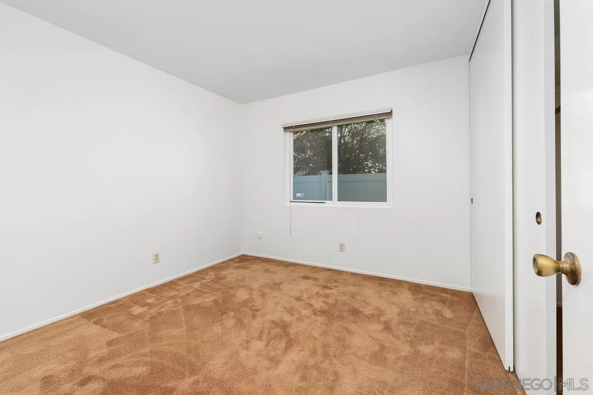 Empty bedroom with tan carpet, white walls, and a window overlooking a fenced yard.