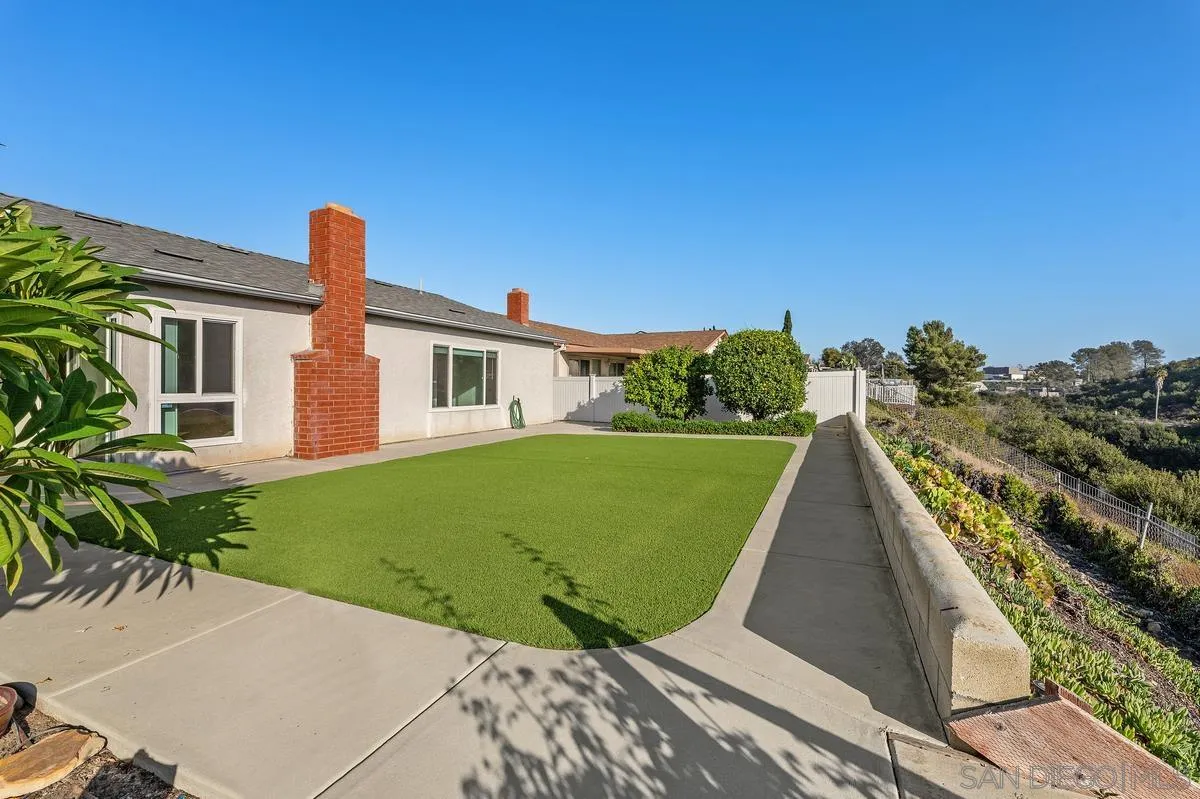 Backyard with artificial turf, a concrete patio, and a brick chimney along the rear of the home.