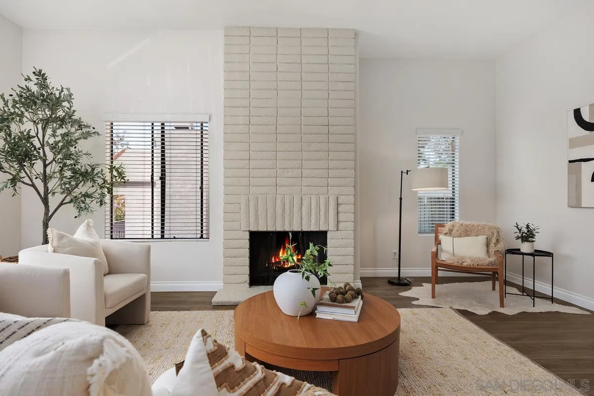 Staged living room with a white brick fireplace, cream seating, and a round wood coffee table.