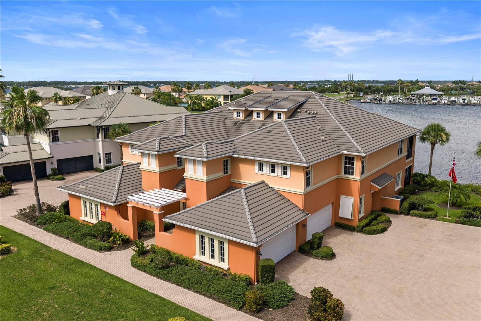 Orange two-story waterfront residence with a tiled roof, marina, and neighboring homes.