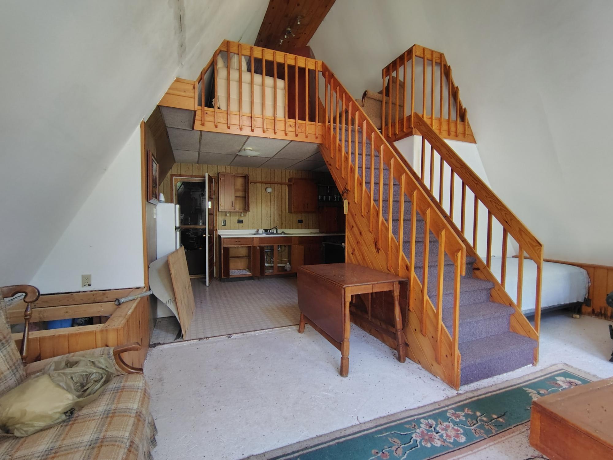 Furnished loft with a small kitchen, open sleeping area, and carpeted staircase with wooden railings.