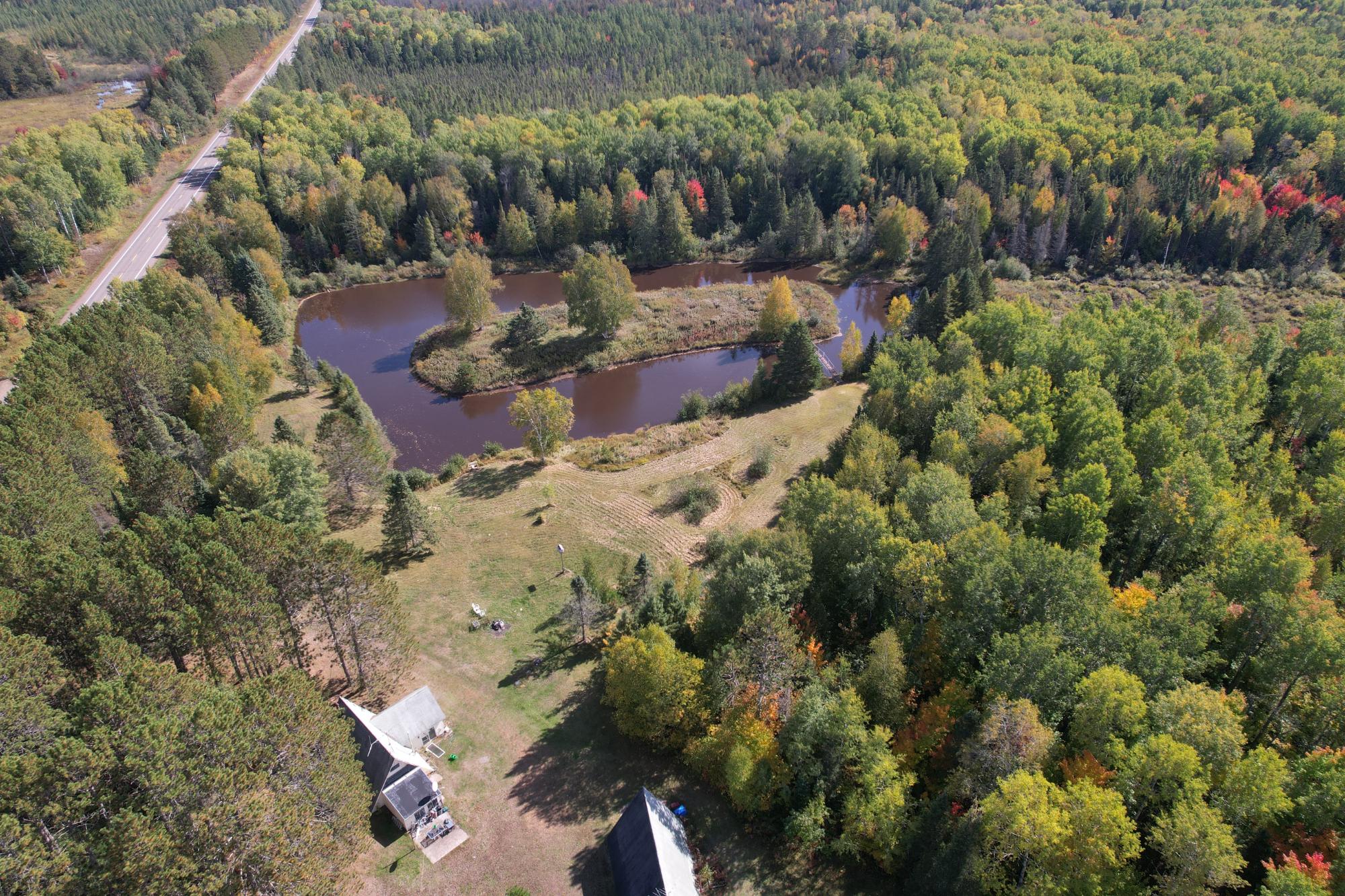 Aerial view of a wooded property with a winding pond, open lawn, and buildings.