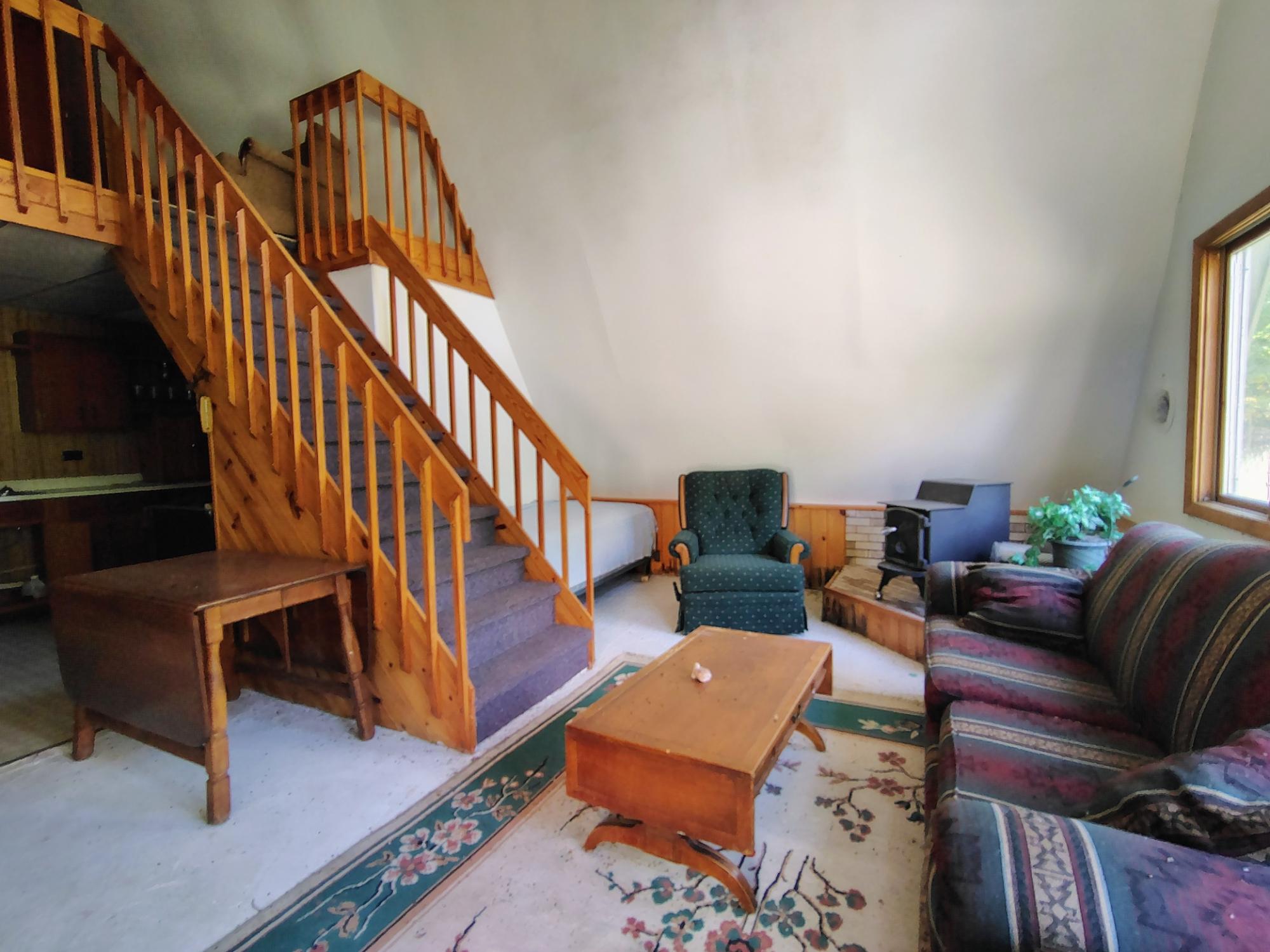 Living room with a wooden staircase, loft railing, patterned sofa, and large window.