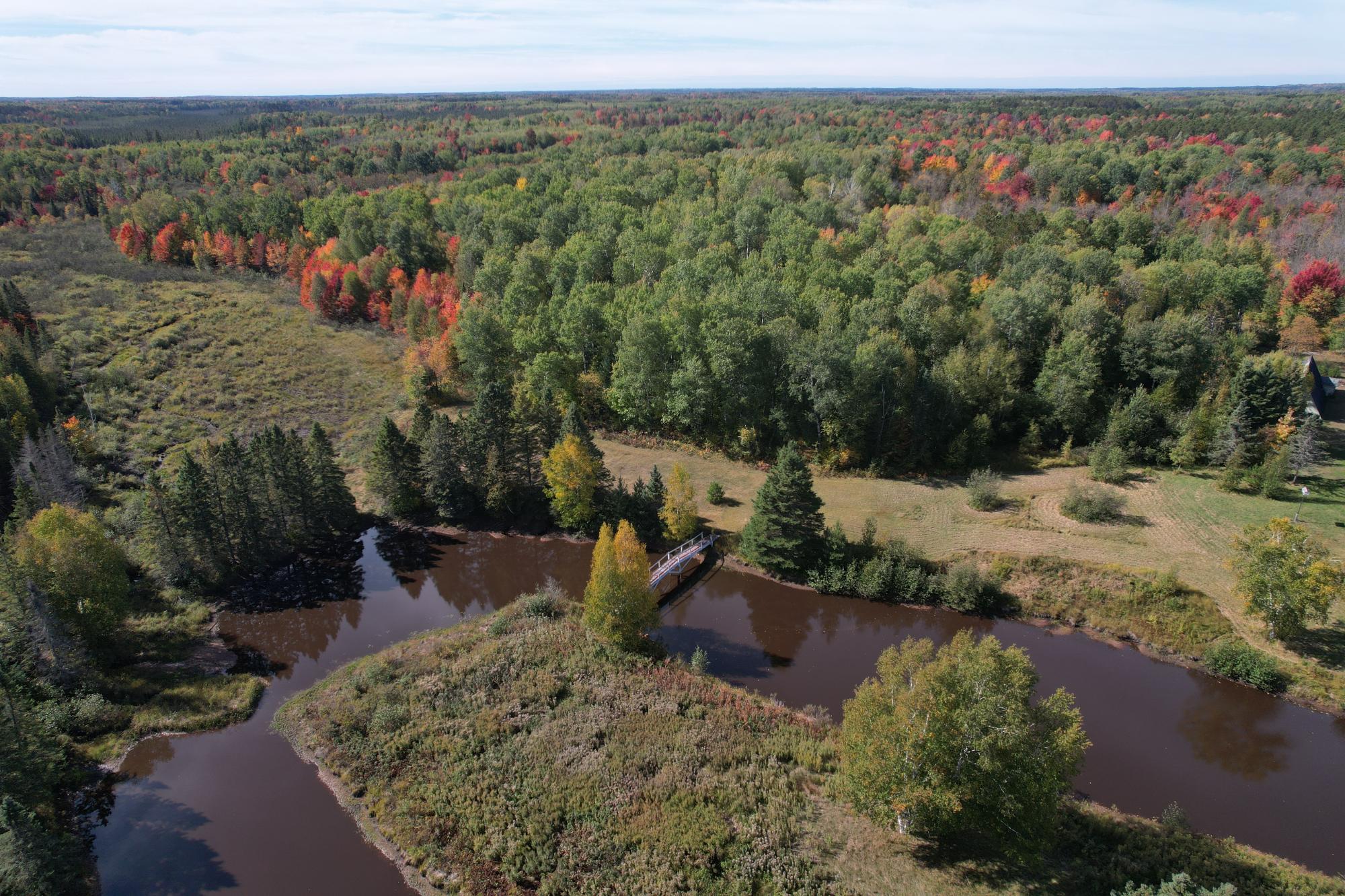 Aerial view of wooded acreage with a winding river and small bridge amid autumn foliage.