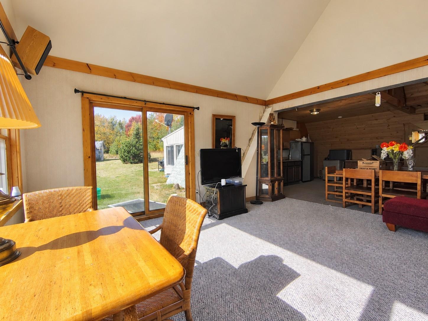 Open living and dining area with vaulted ceiling, wood trim, and sliding glass doors overlooking fall foliage.