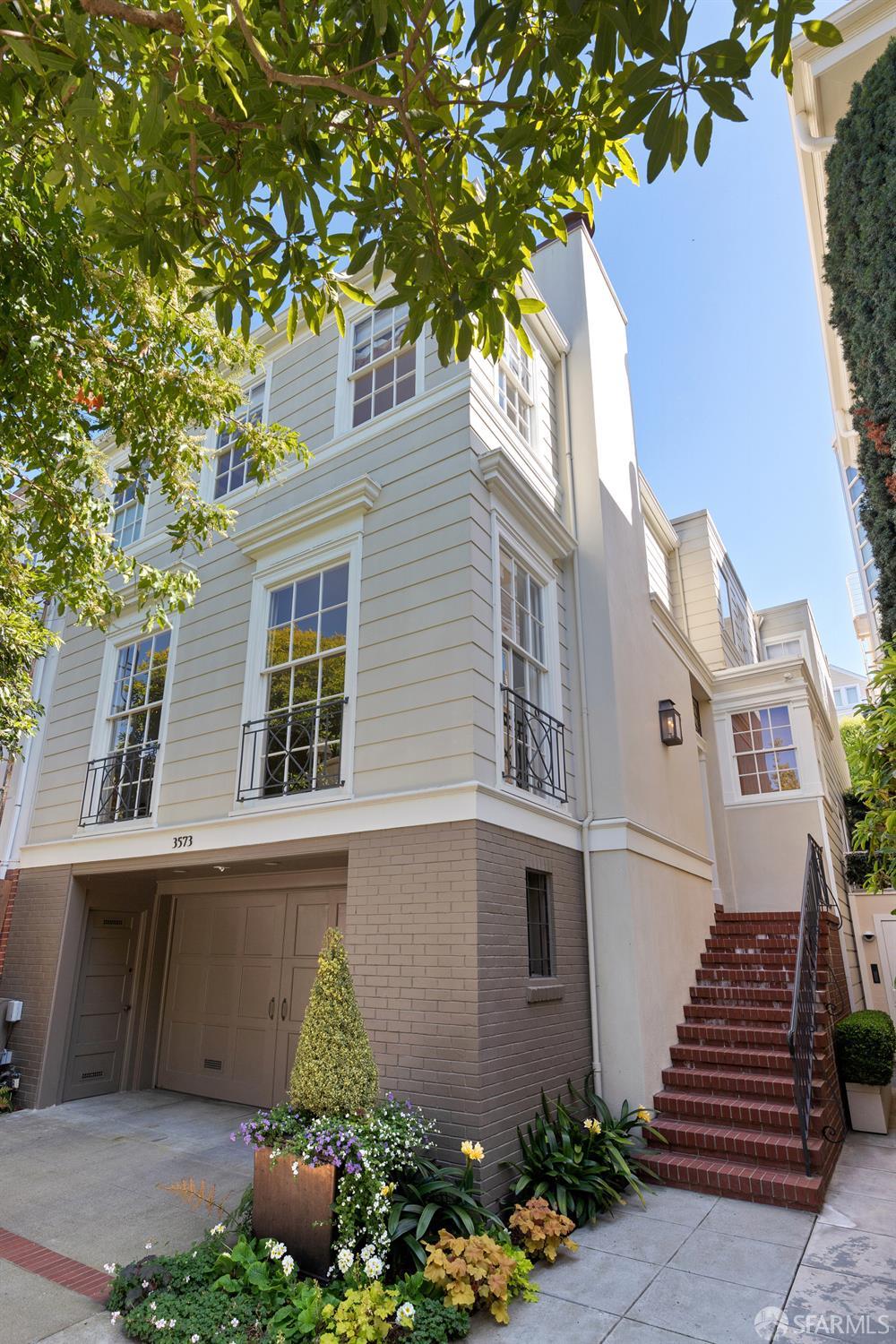 Multi-story light-colored home with a garage, brick steps, and leafy trees; number 3573 is above the garage.