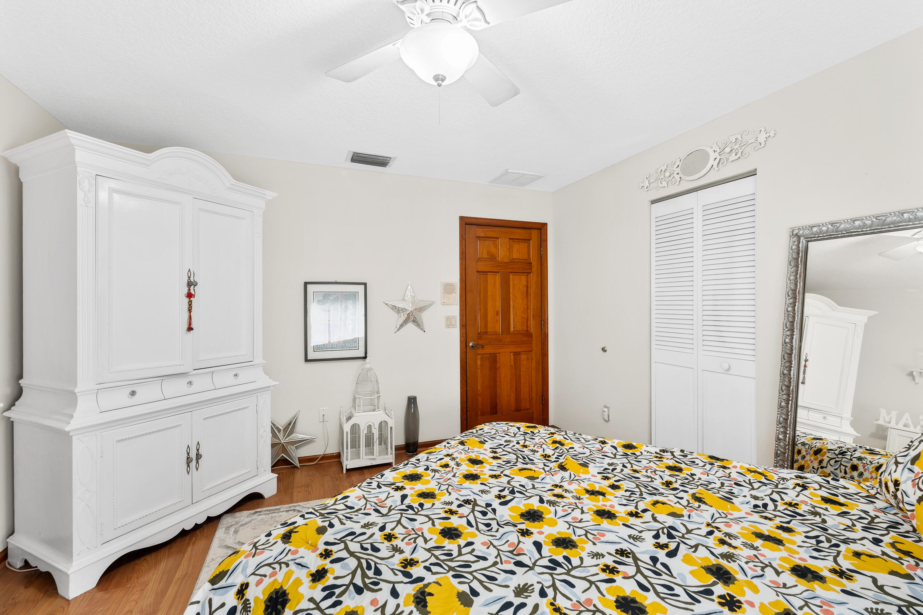 Bedroom with yellow floral bedding, a large white wardrobe, and a full-length mirror.