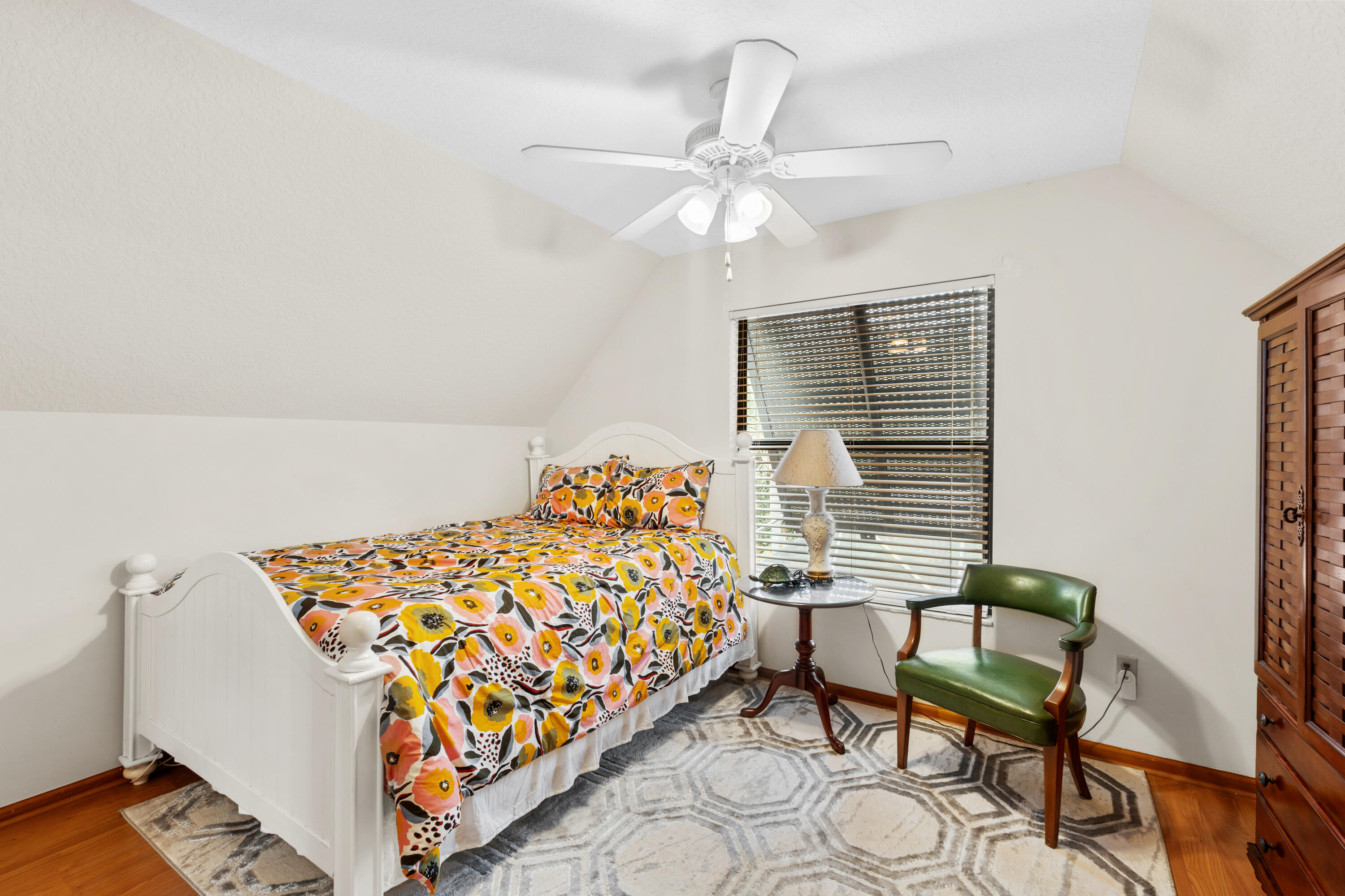 Bedroom with colorful floral bedding, a green leather chair, and a geometric-patterned rug.