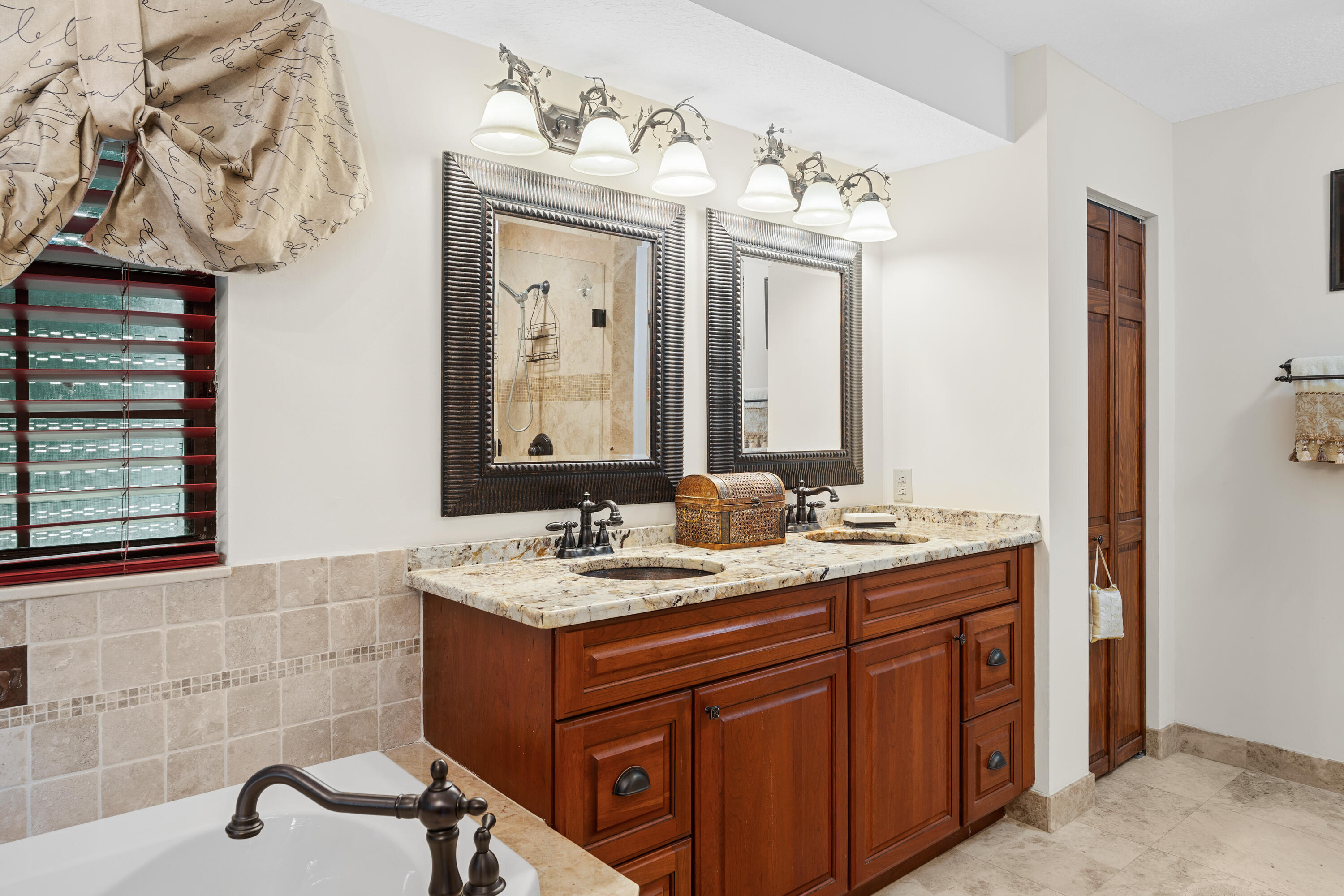 Bathroom with a cherry-wood double vanity, marble countertop, framed mirrors, and bathtub.