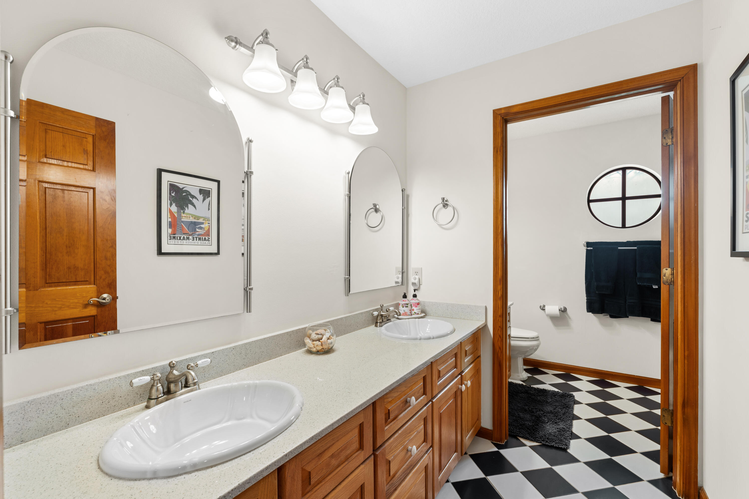 Bathroom with a double-sink wood vanity and adjoining toilet area with checkerboard tile.