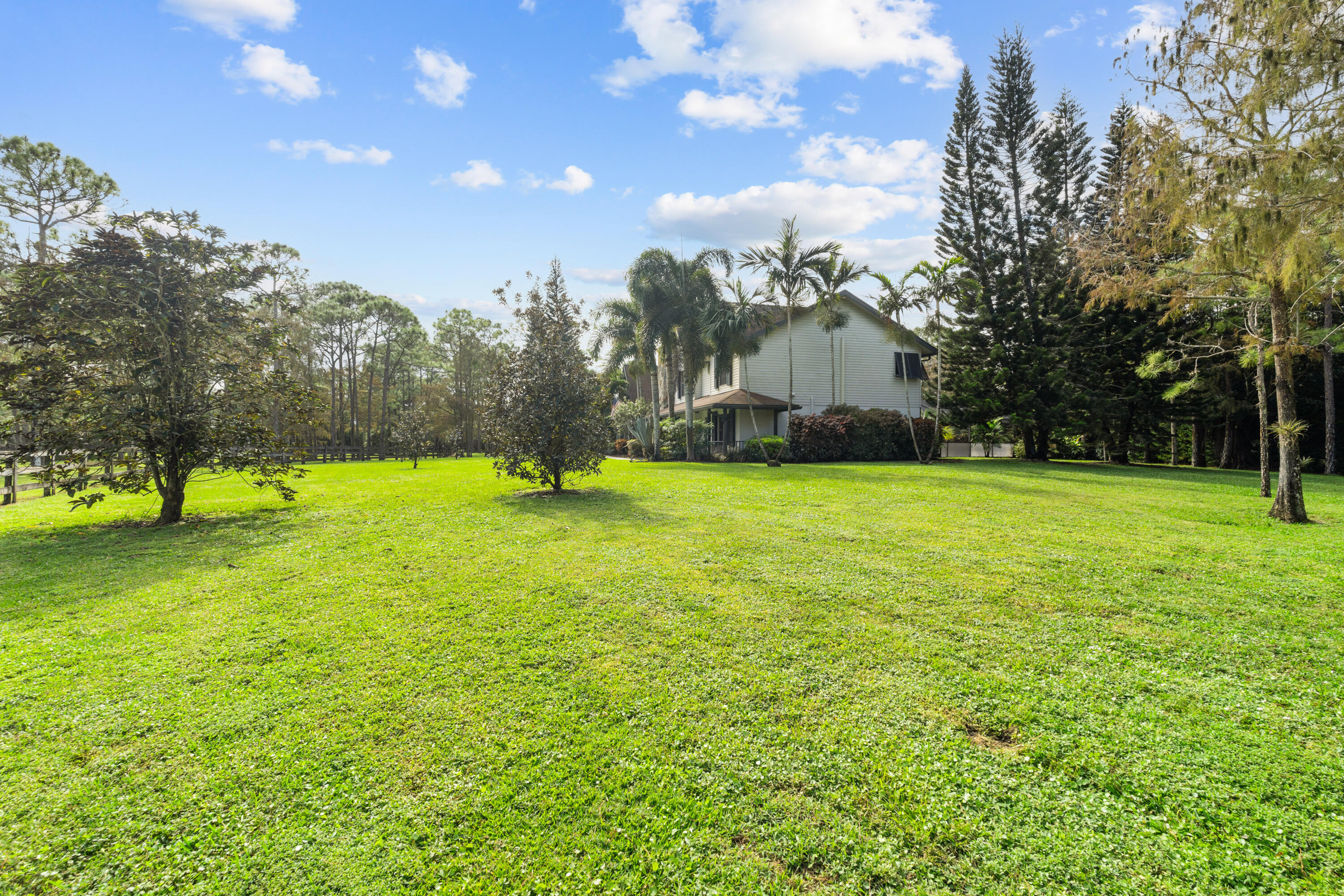 Two-story house beyond a broad green lawn, framed by palms and mature trees.