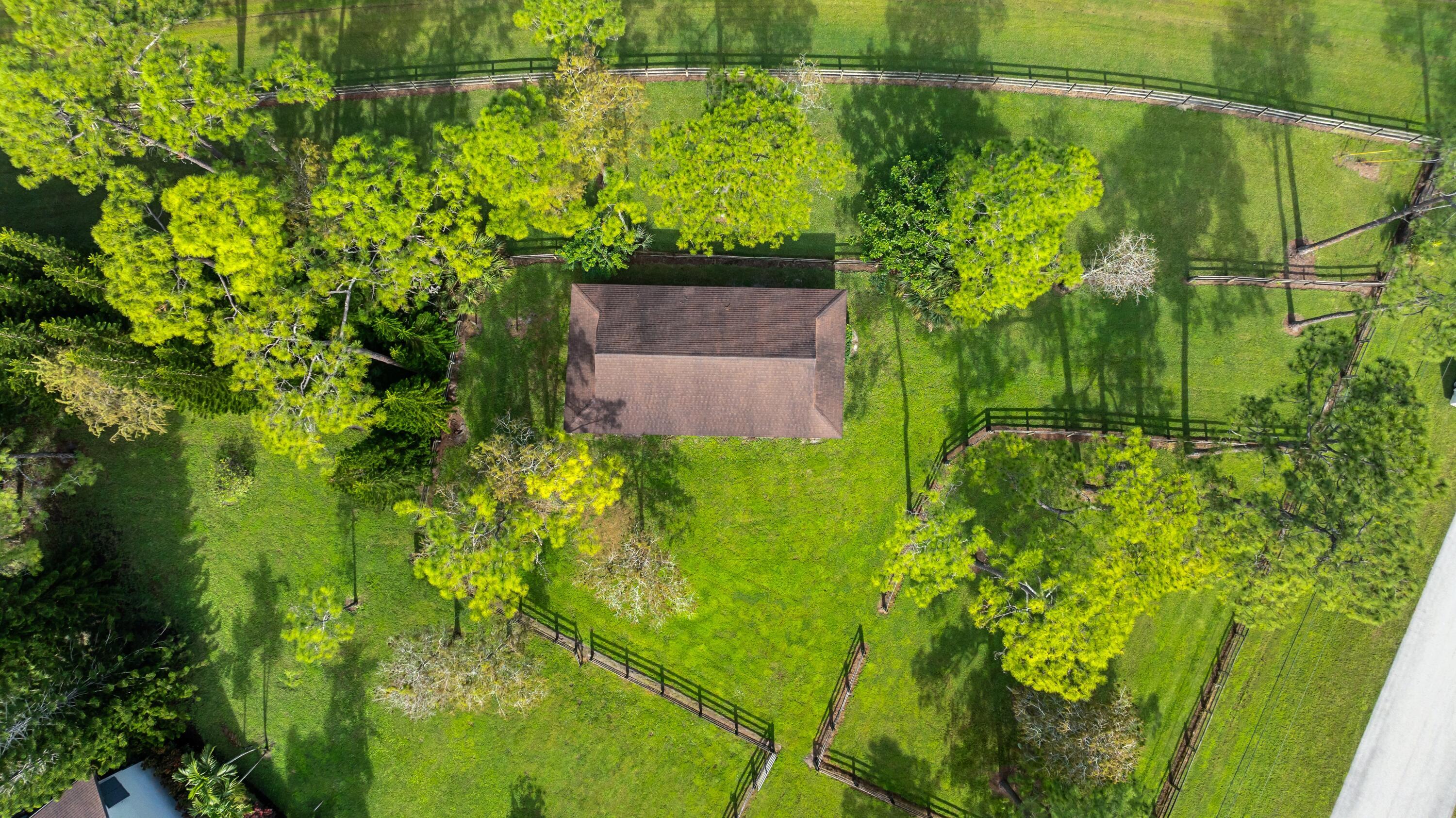 Aerial view of fenced grassy paddocks and a roofed structure among mature trees.