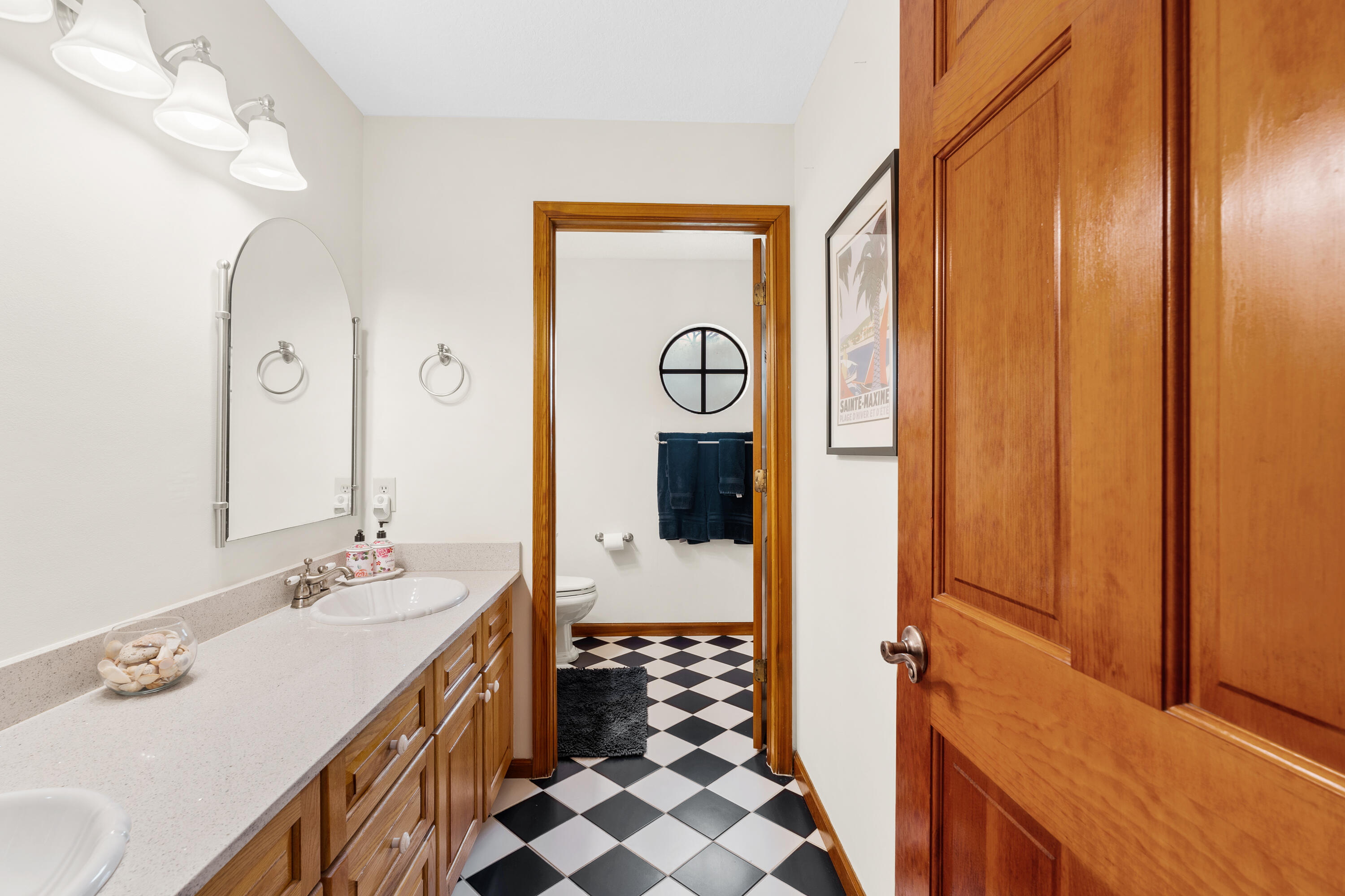 Bathroom with a wood vanity and pale counter leading to a checkerboard-floored toilet area.