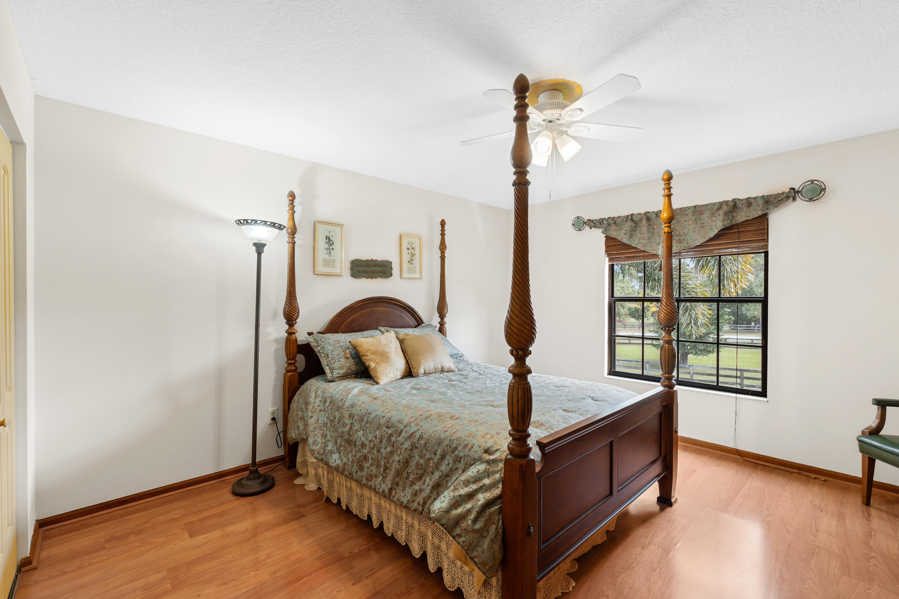 Bedroom with a carved four-poster bed, patterned bedding, and a large window overlooking greenery.