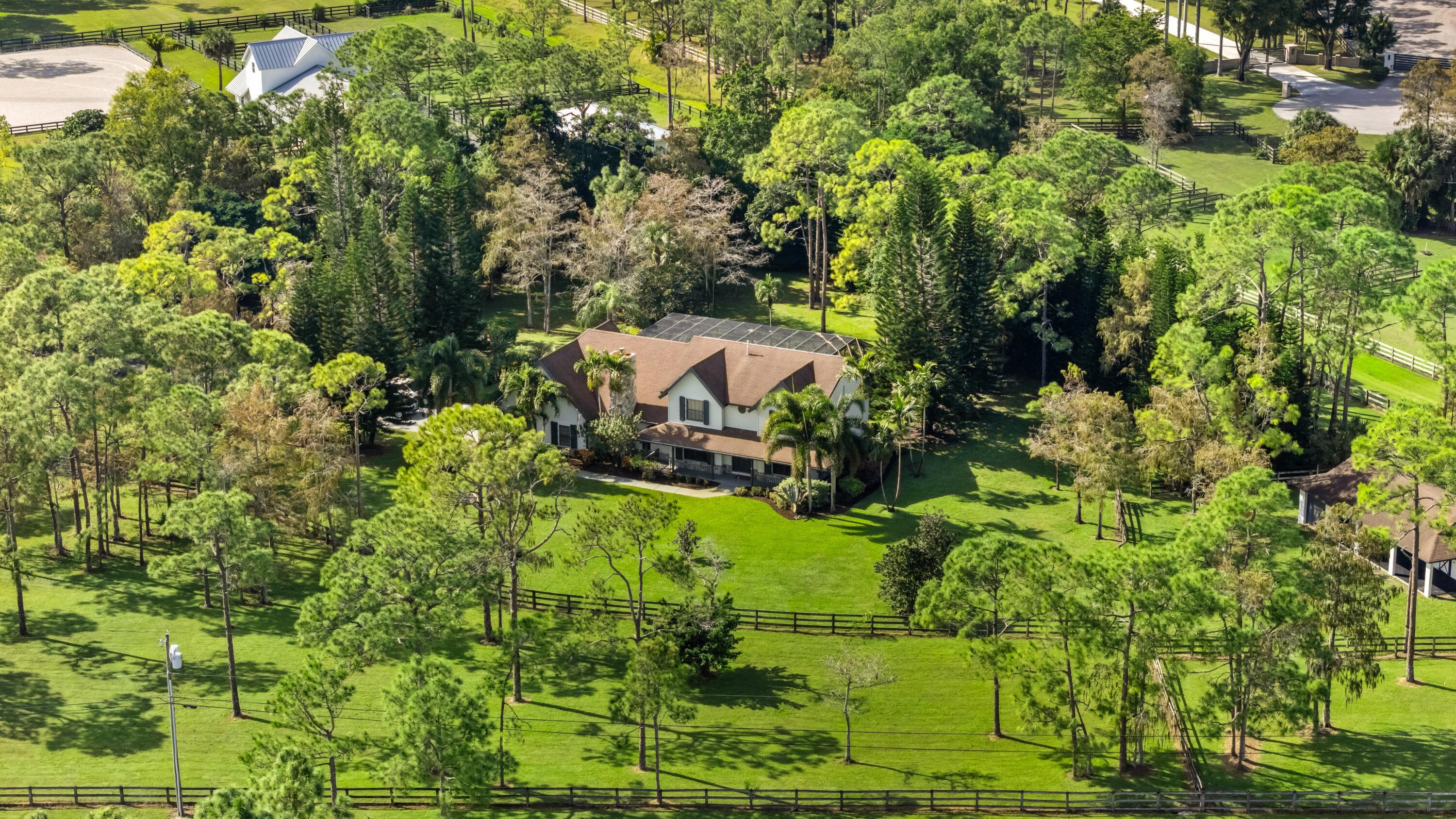 Aerial view of a large home amid fenced green lawns and mature trees.