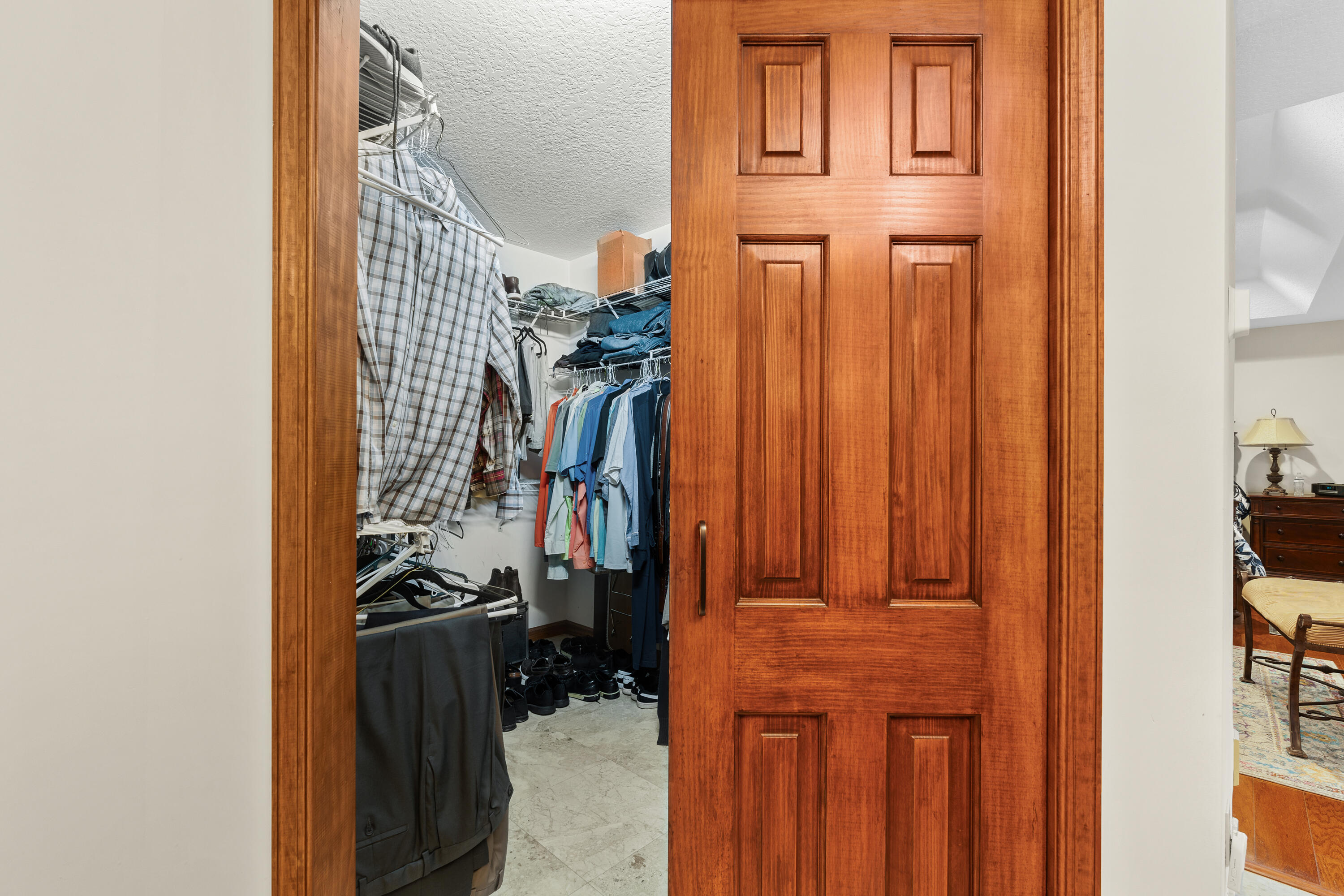 Walk-in closet with hanging clothes, storage shelves, and shoes, viewed through a partially open wooden door.