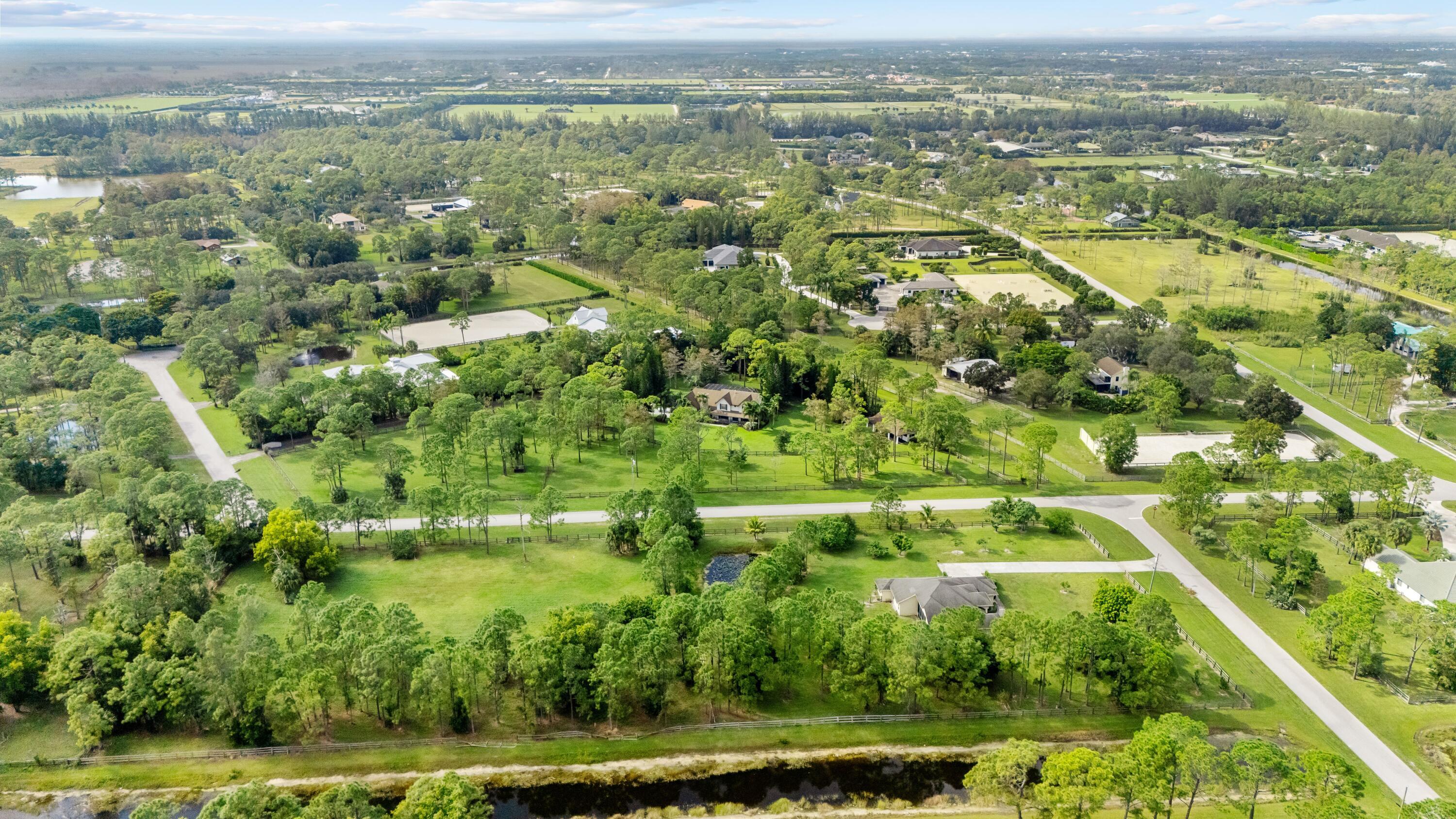 Aerial view of wooded equestrian properties with fenced paddocks, riding arenas, and a canal.