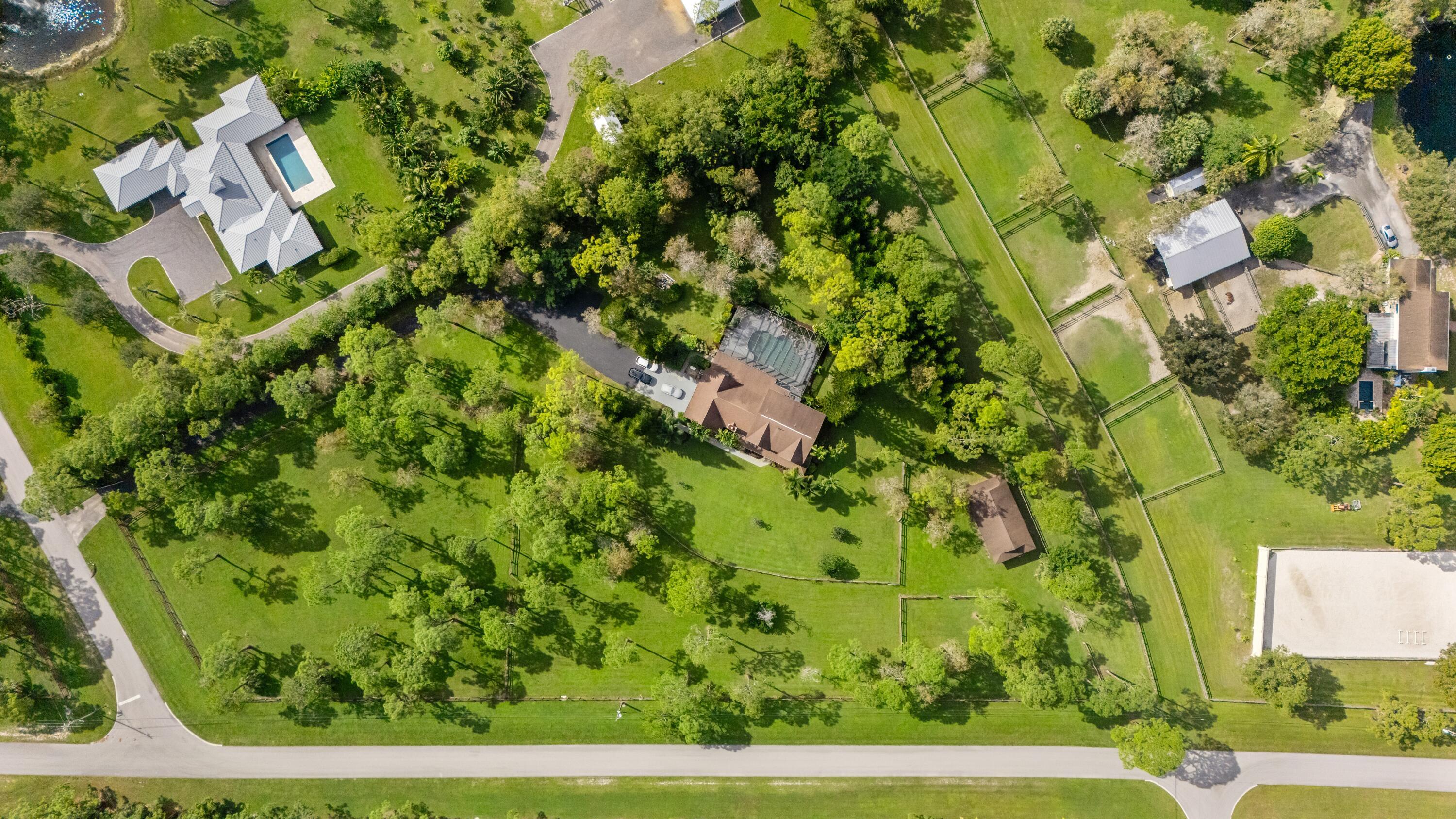 Aerial view of an equestrian estate with fenced paddocks, a tree-shaded home, and a riding arena.