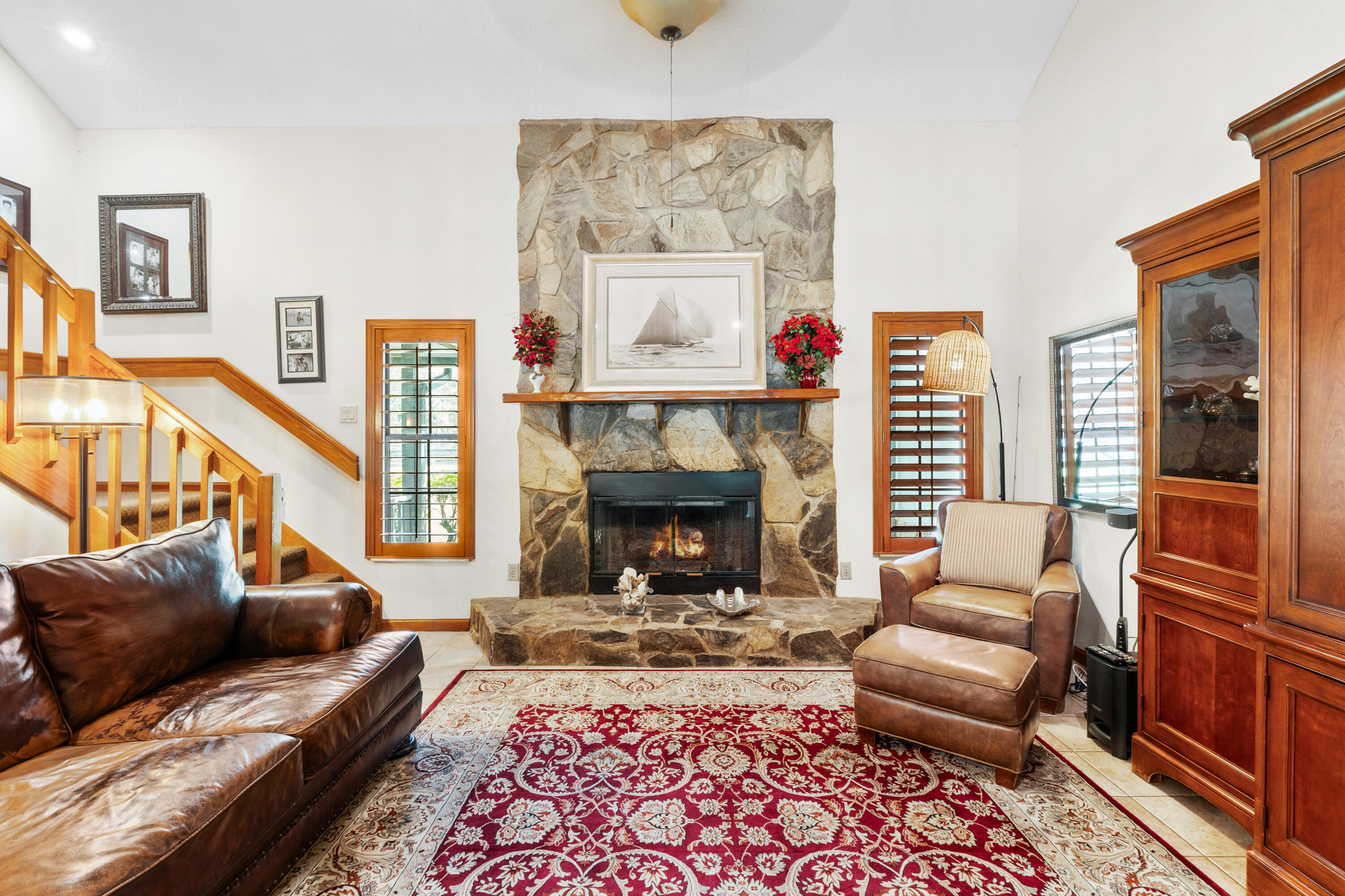 Living room with a stone fireplace, leather seating, and a red patterned rug.