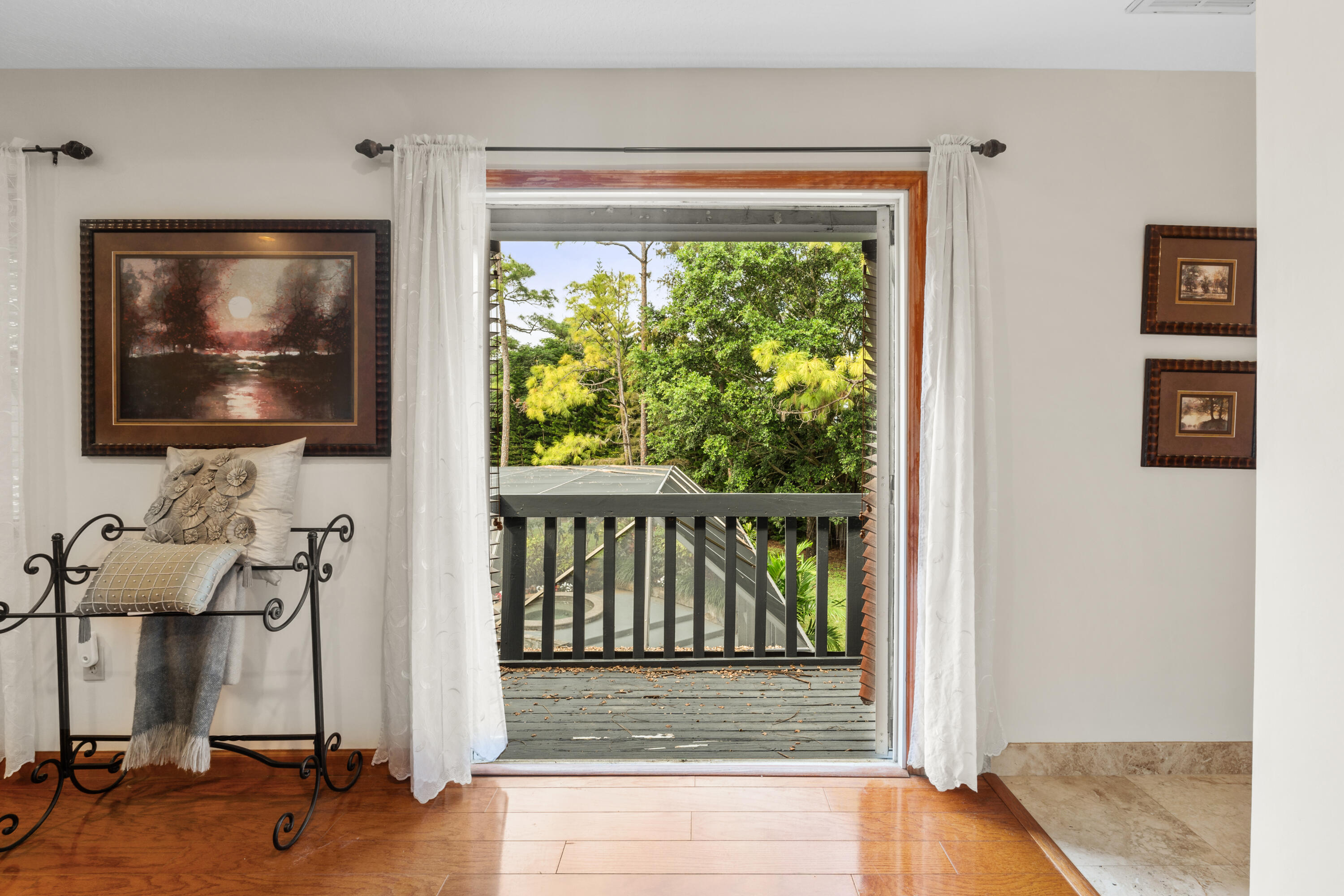 Furnished room opens onto a wood deck overlooking leafy trees, with a partial pool view below.