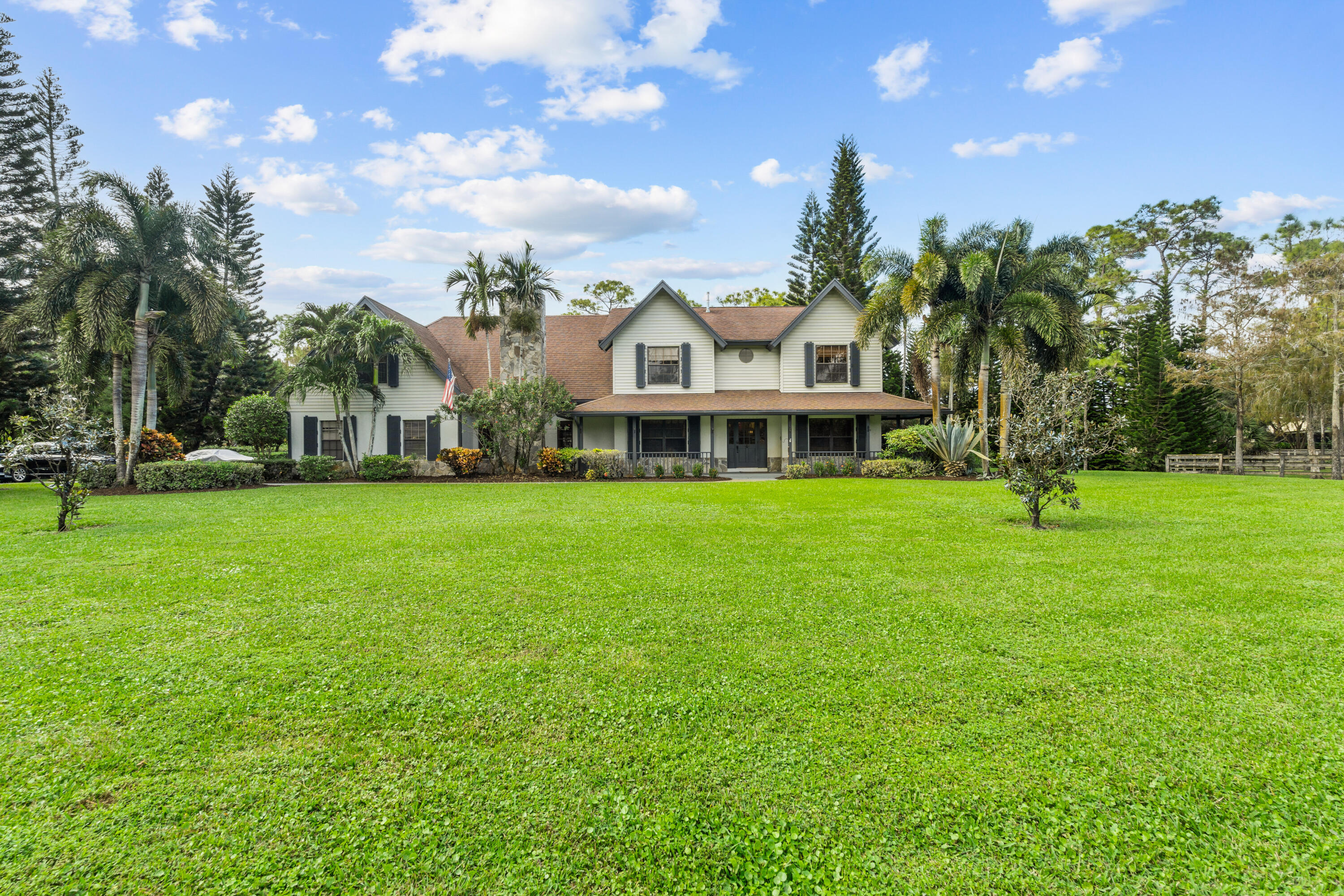 Two-story home with a broad green lawn, covered porch, and mature palms.