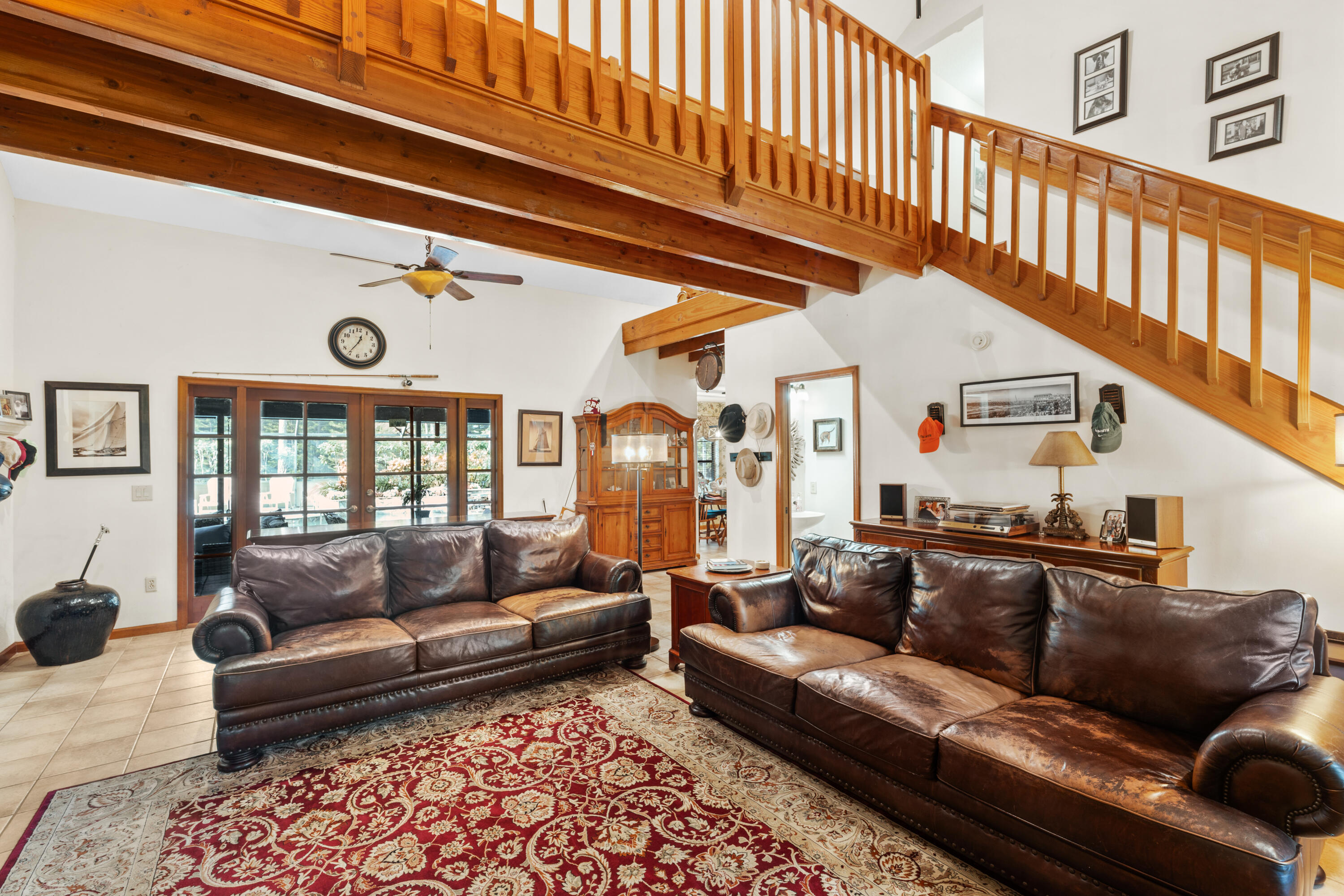 Living room with leather sofas, a patterned rug, and a prominent wooden mezzanine staircase.