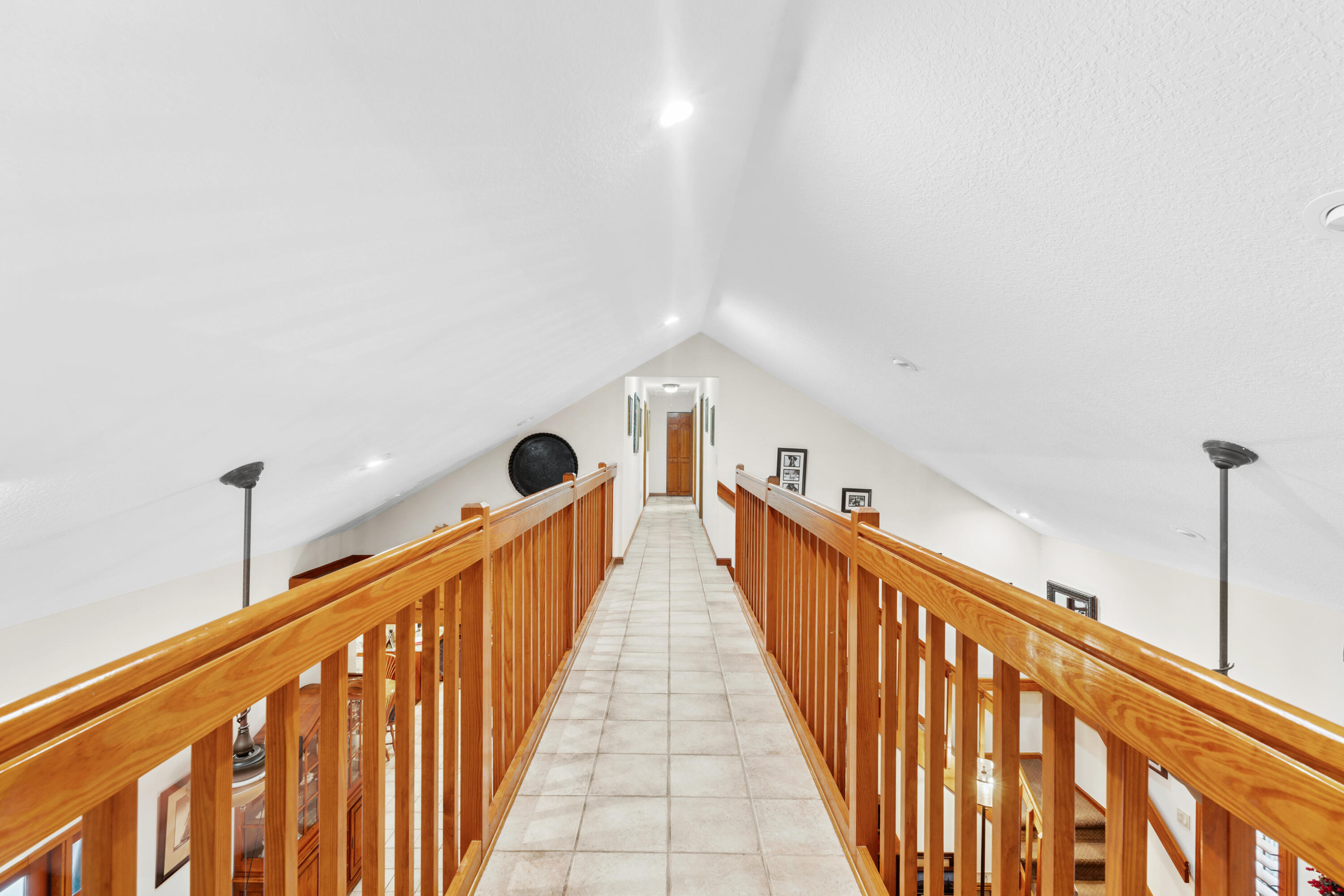 Upstairs loft walkway with tiled flooring, wooden railings, and a vaulted ceiling.