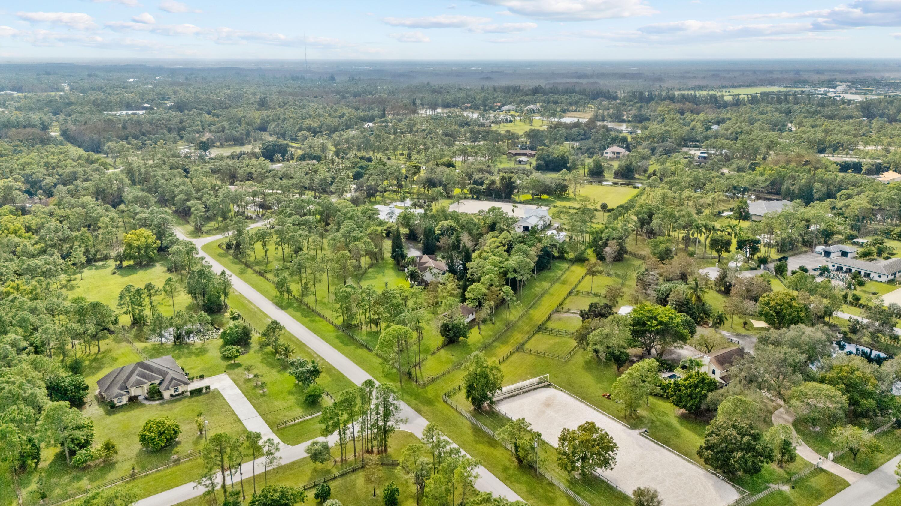 Equestrian property with fenced paddocks and a large riding arena amid mature trees.